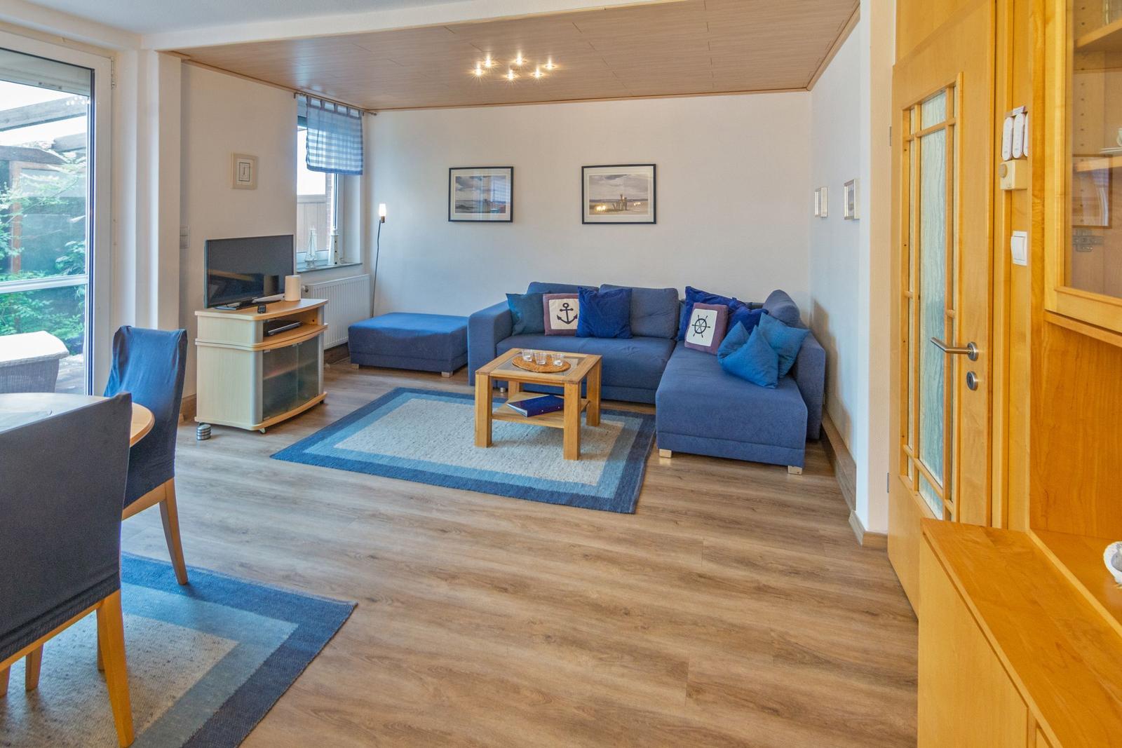 Wohnzimmer mit blauem Sofa, Holzboden und TV. Durchgang zur Küche.