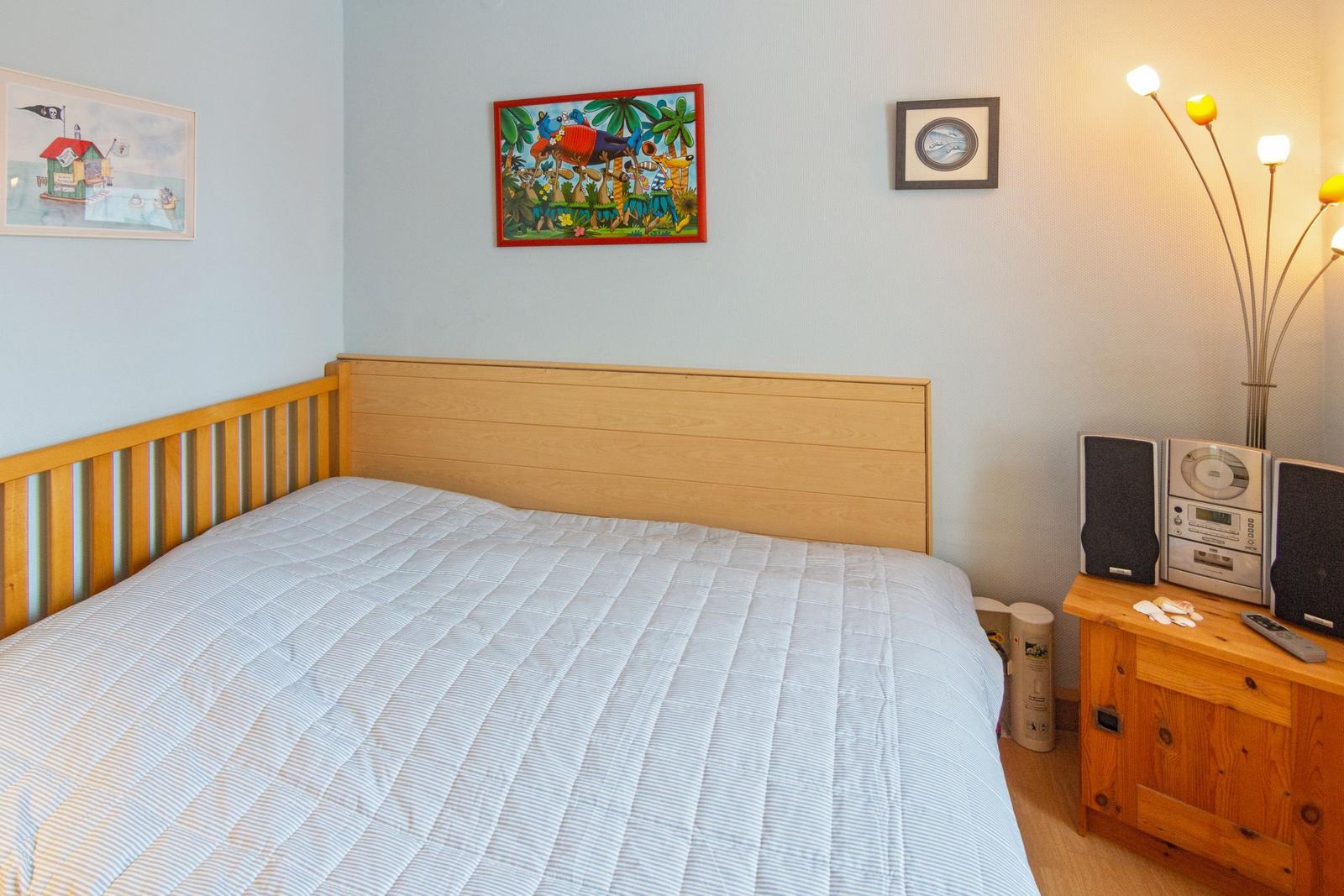 Ein Schlafzimmer mit einem Bett, Wandbildern und einem Holzschrank mit Stereoanlage.