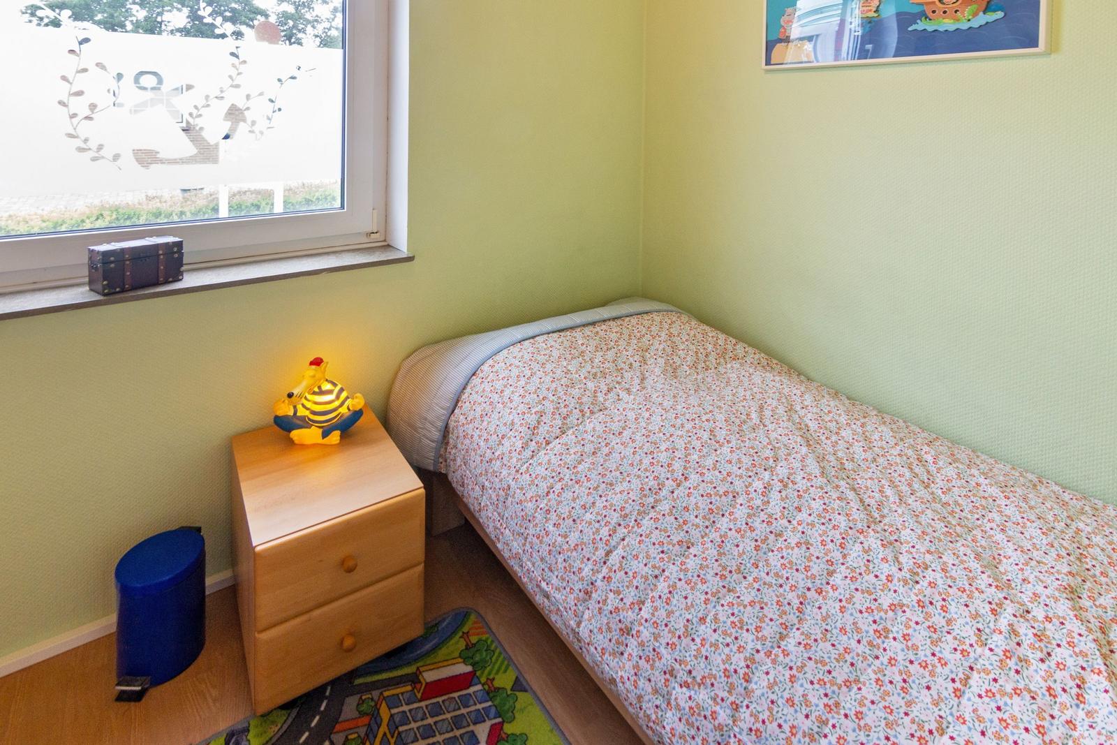 Ein Schlafzimmer mit Bett, Nachttisch und Fenster. Wandfarbe ist hellgrün.
