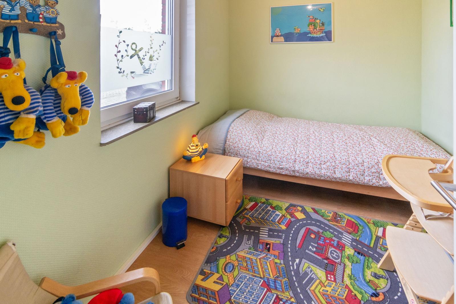 Kinderzimmer mit Bett, Schreibtisch, Spielteppich und Fenster