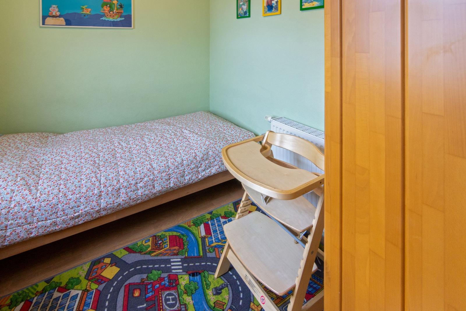 Ein Kinderzimmer mit einem Bett und einem Hochstuhl auf einem Spielteppich.