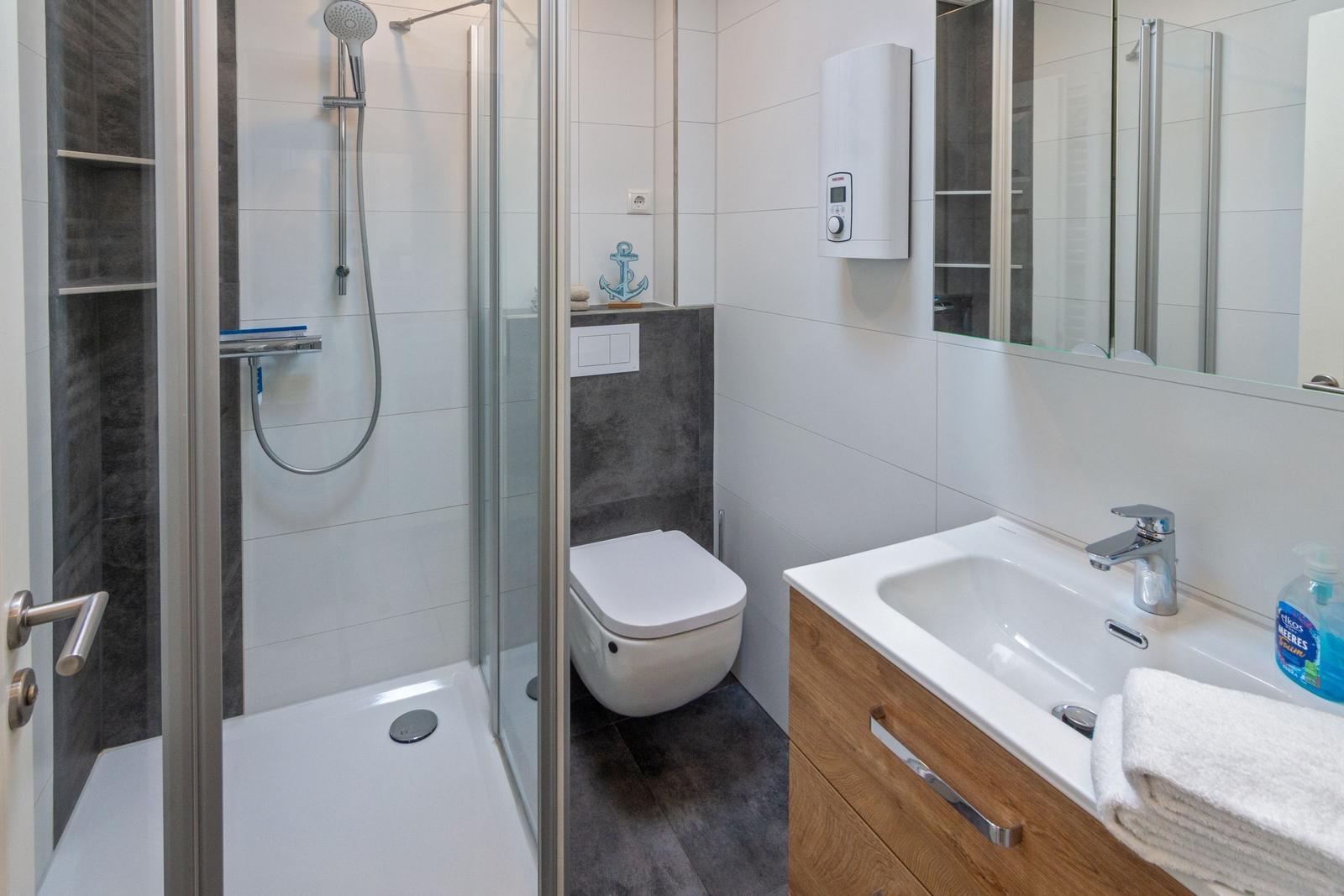 Badezimmer mit Dusche, Toilette und Waschbecken mit Spiegel.