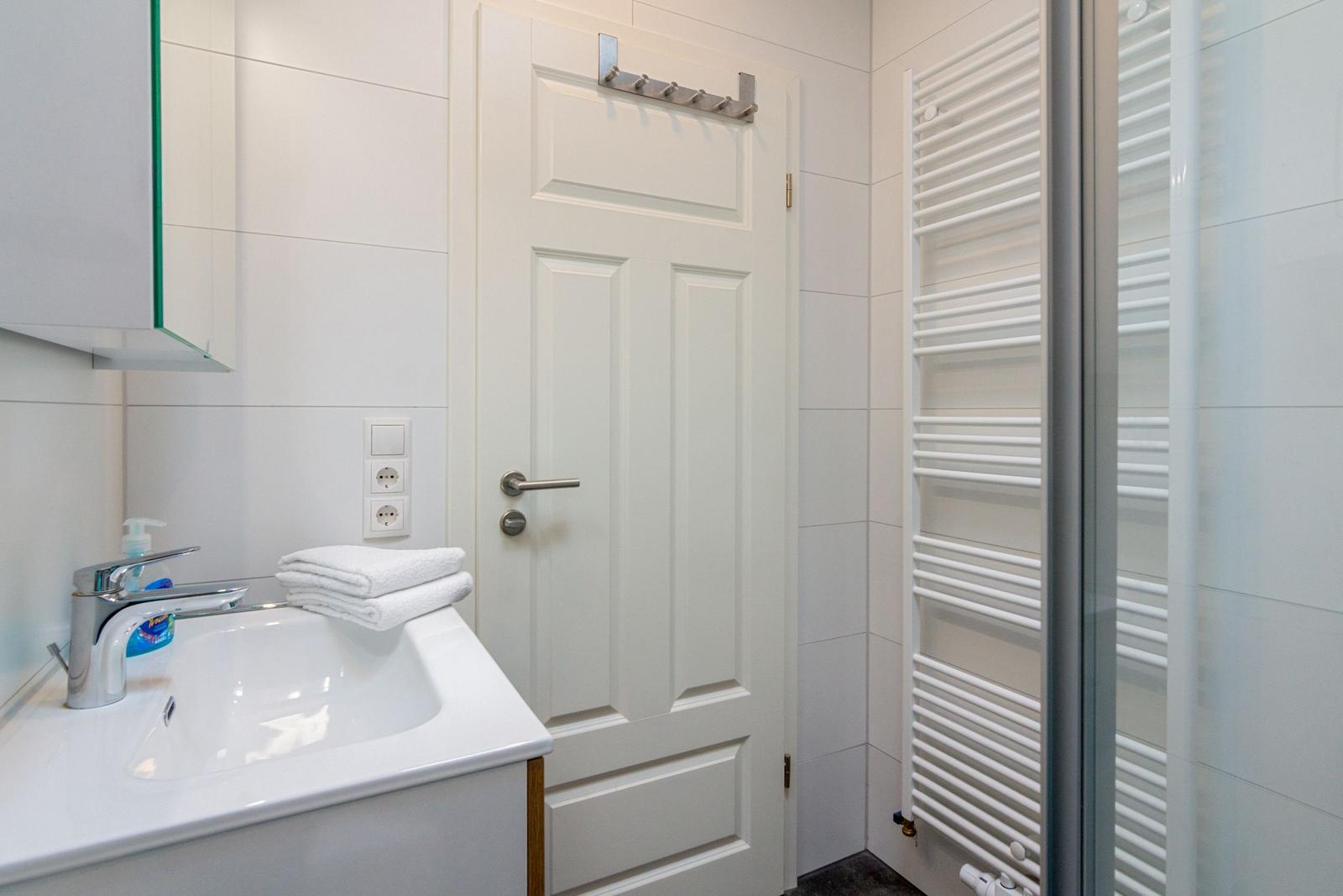 Badezimmer mit Waschbecken, Spiegelschrank und Duschbereich mit Heizkörper.