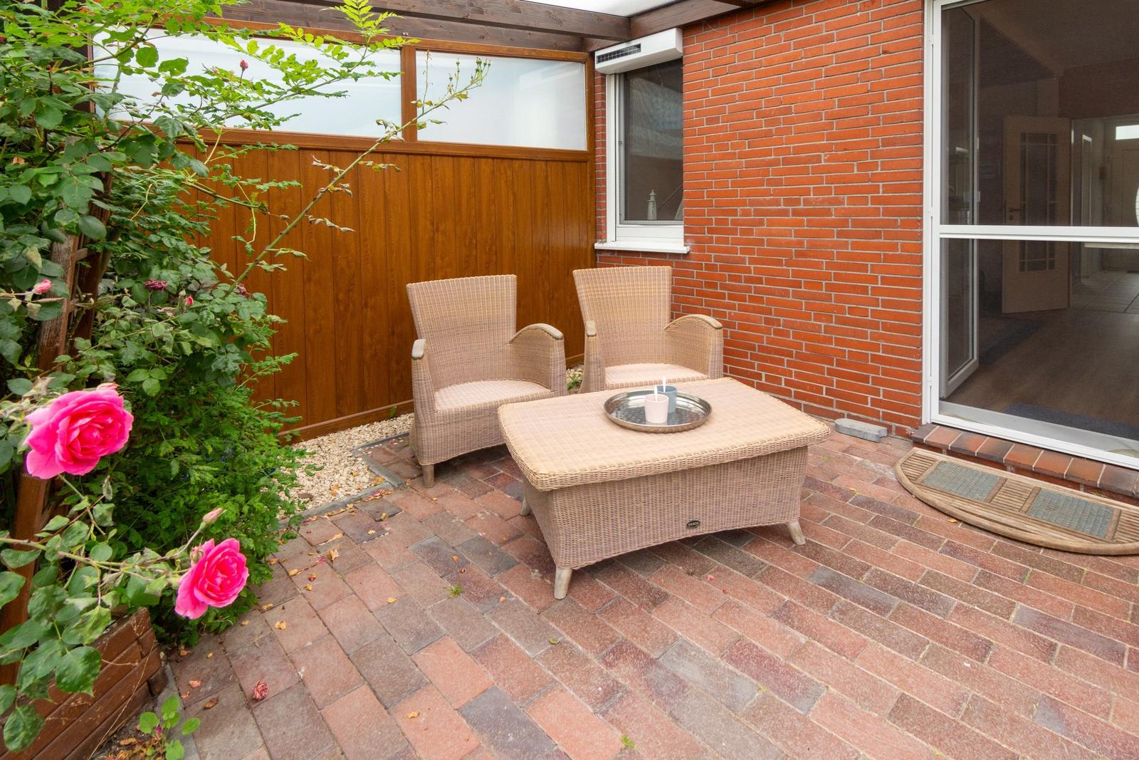 Terrasse mit zwei Stühlen und Tisch, roten Ziegel und rosa Rosen.