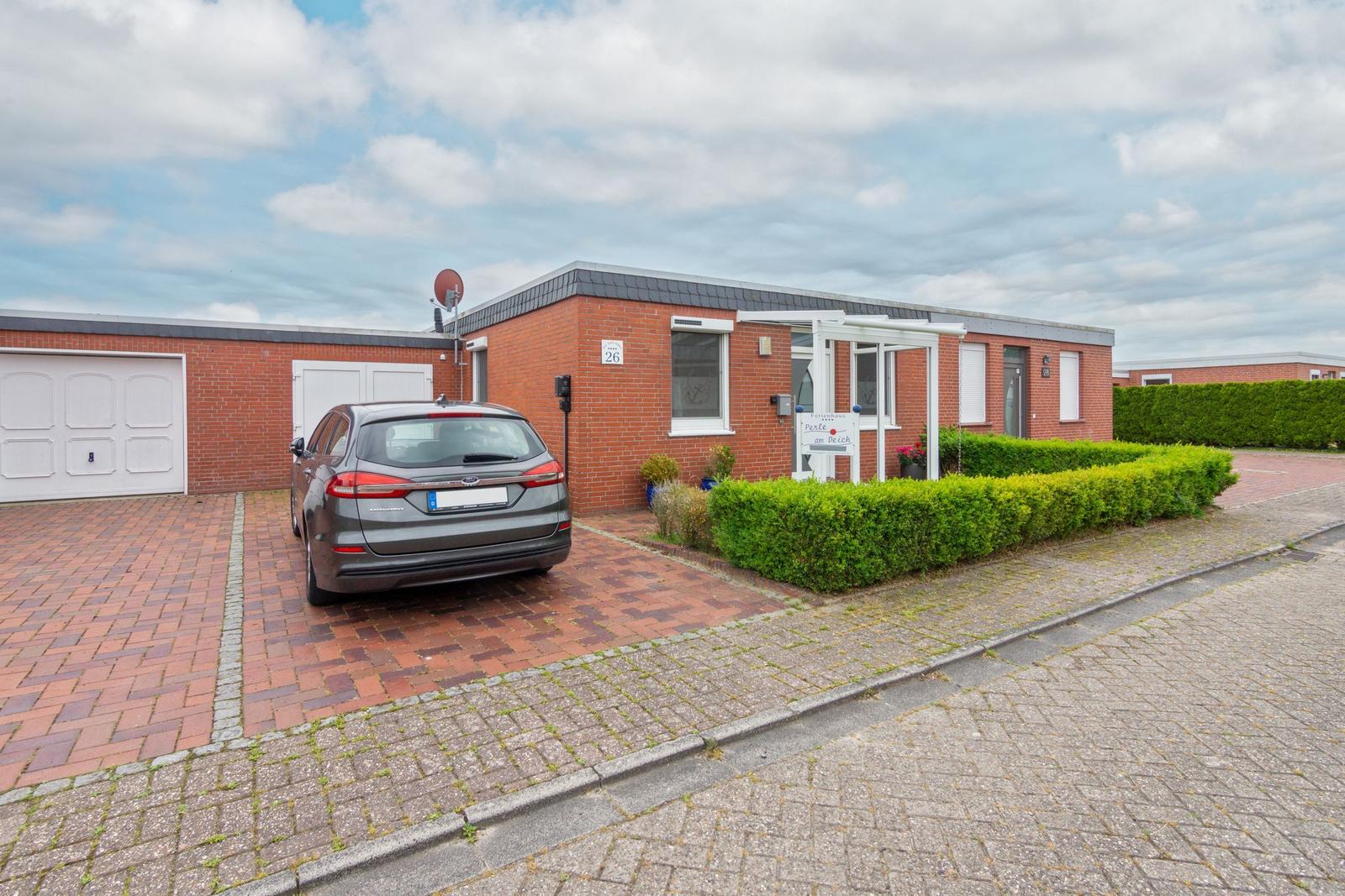 Rotes Backsteingebäude mit Garage und gepflastertem Vorplatz. Ein Auto parkt vor dem Eingang.