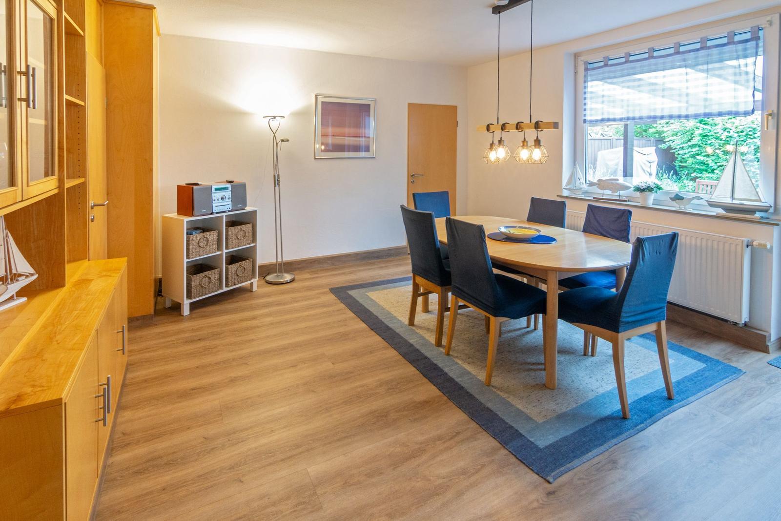Esszimmer mit Holztisch, blauen Stühlen und Fensterblick auf Garten.