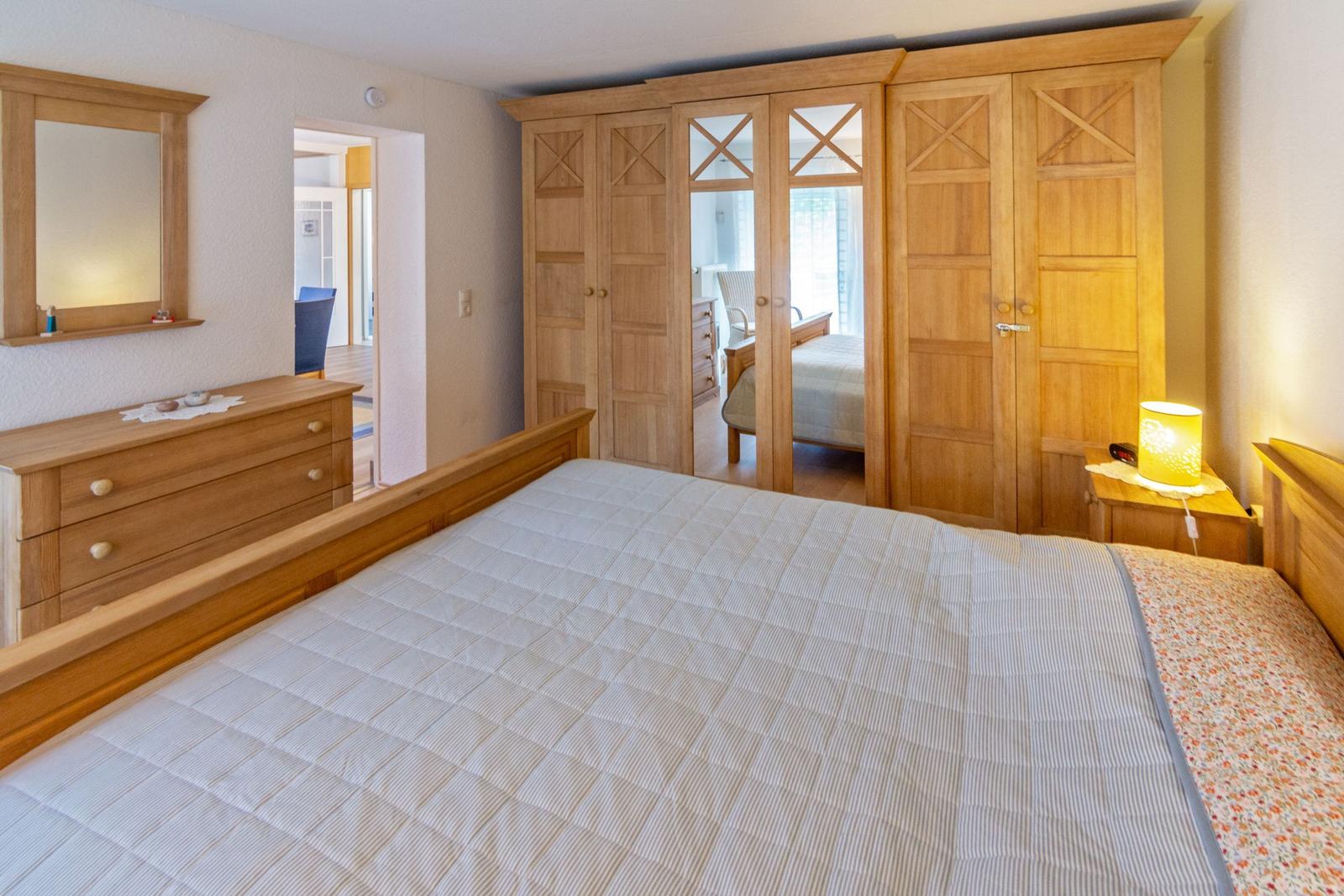 Schlafzimmer mit Holzbett, Schrank und Kommode. Durchgang zu einem weiteren Raum.