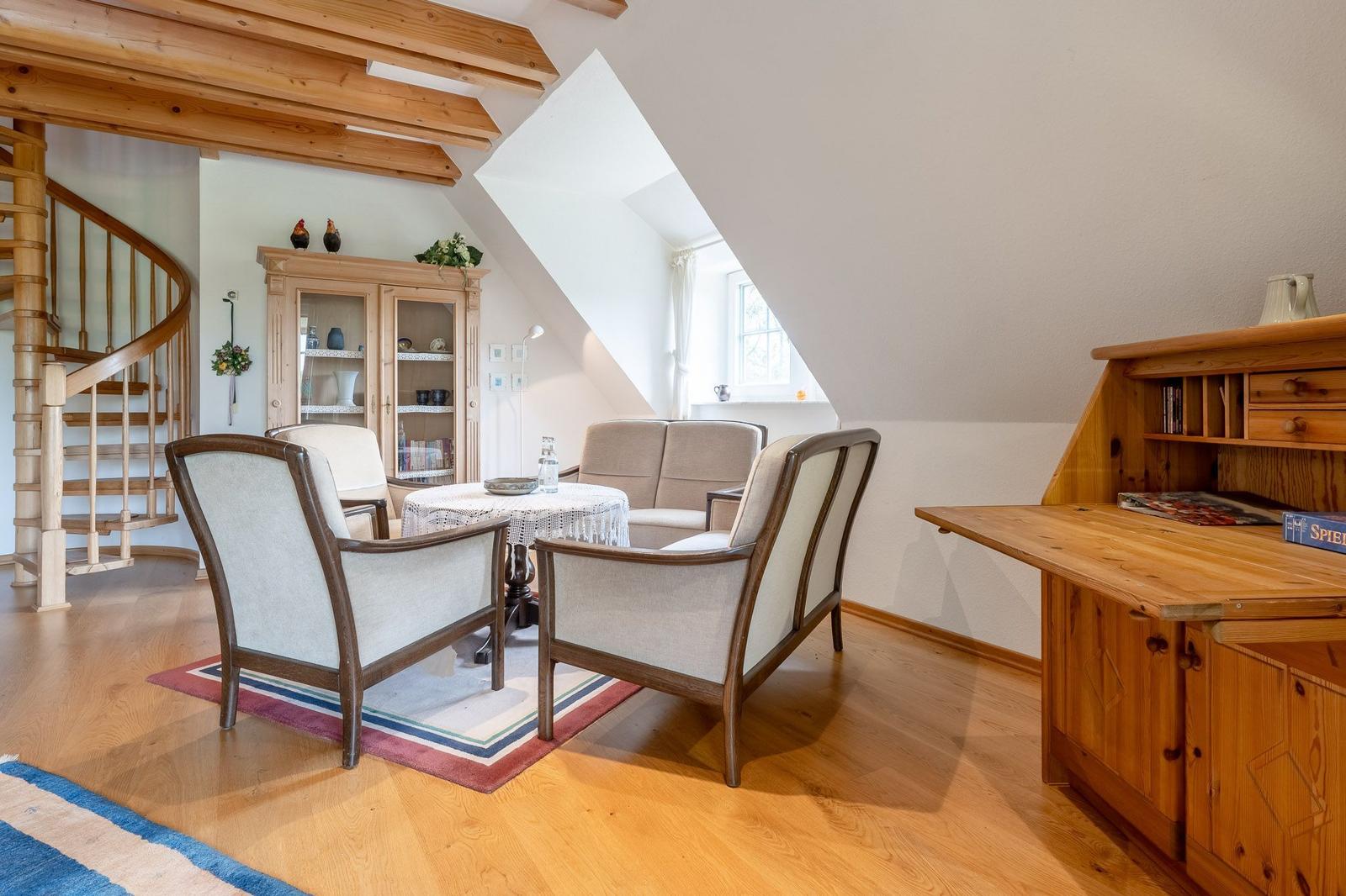 Wohnzimmer mit Sitzgruppe, Schreibtisch und Treppe. Holzdecke und Parkettboden.