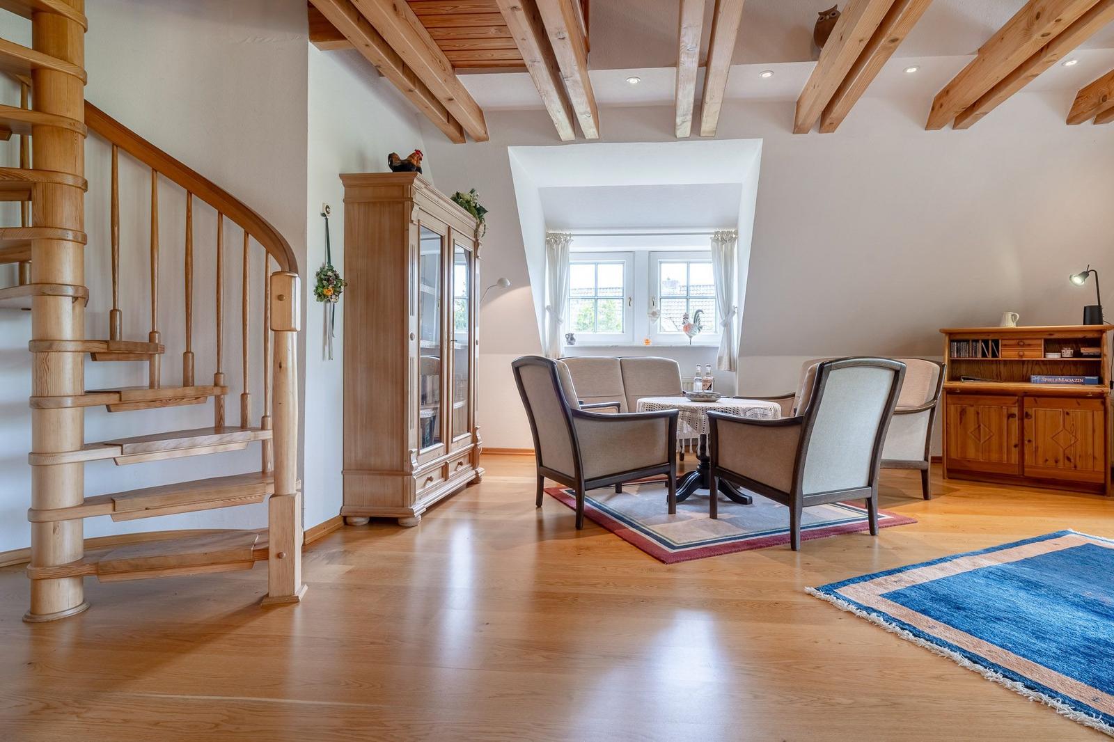 Eingangsbereich mit Holztreppe, Wohnzimmer mit Sitzgruppe und Bücherregal.