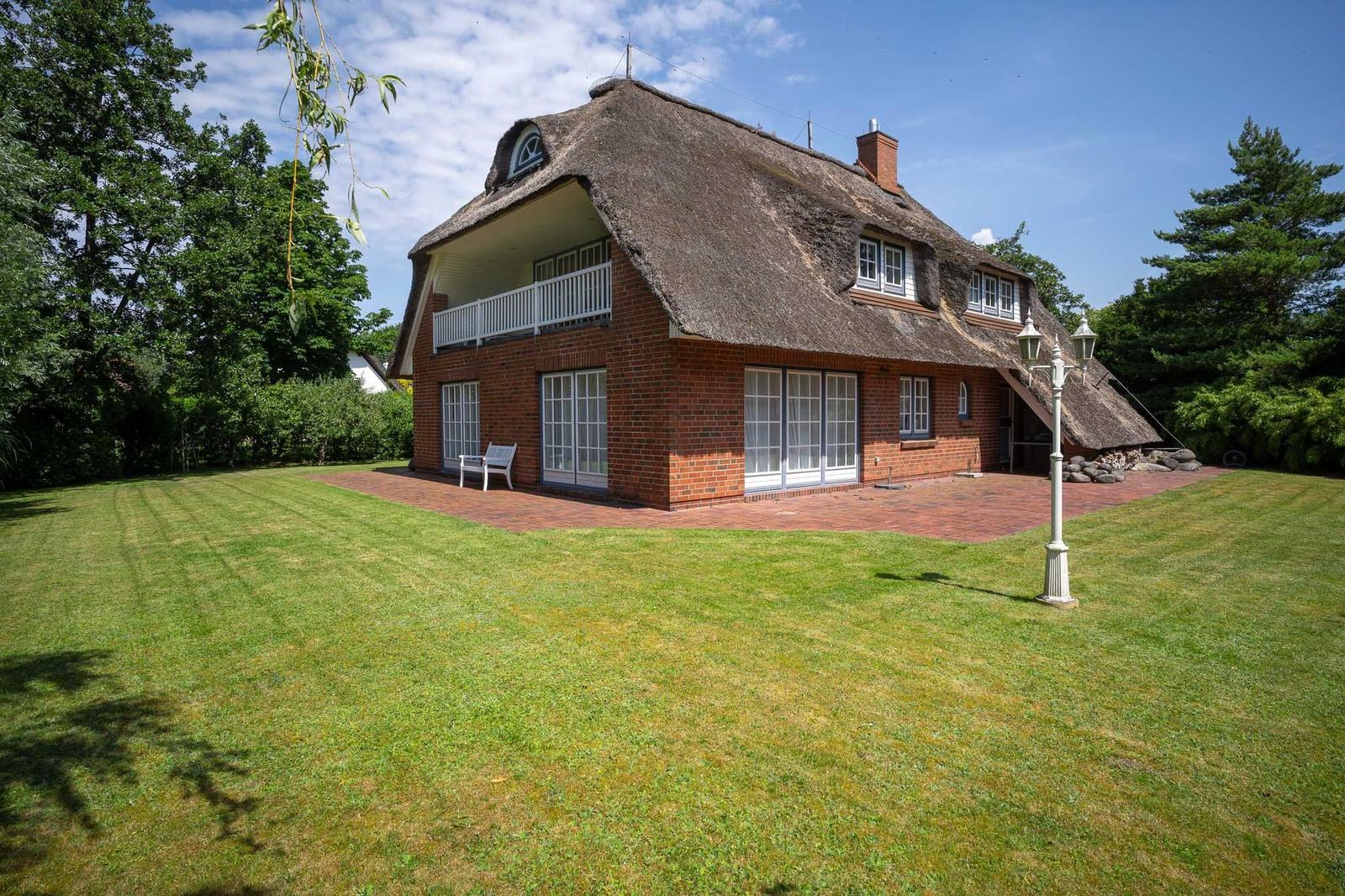 Rotes Backsteinhaus mit Strohdach, weißer Terrasse und grünem Garten.