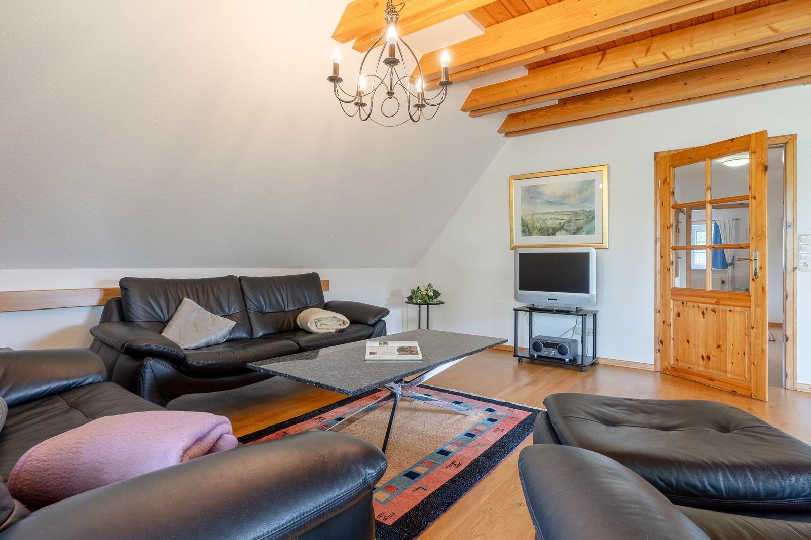 Wohnzimmer mit Ledersofa, Holzdecke und Fernseher.