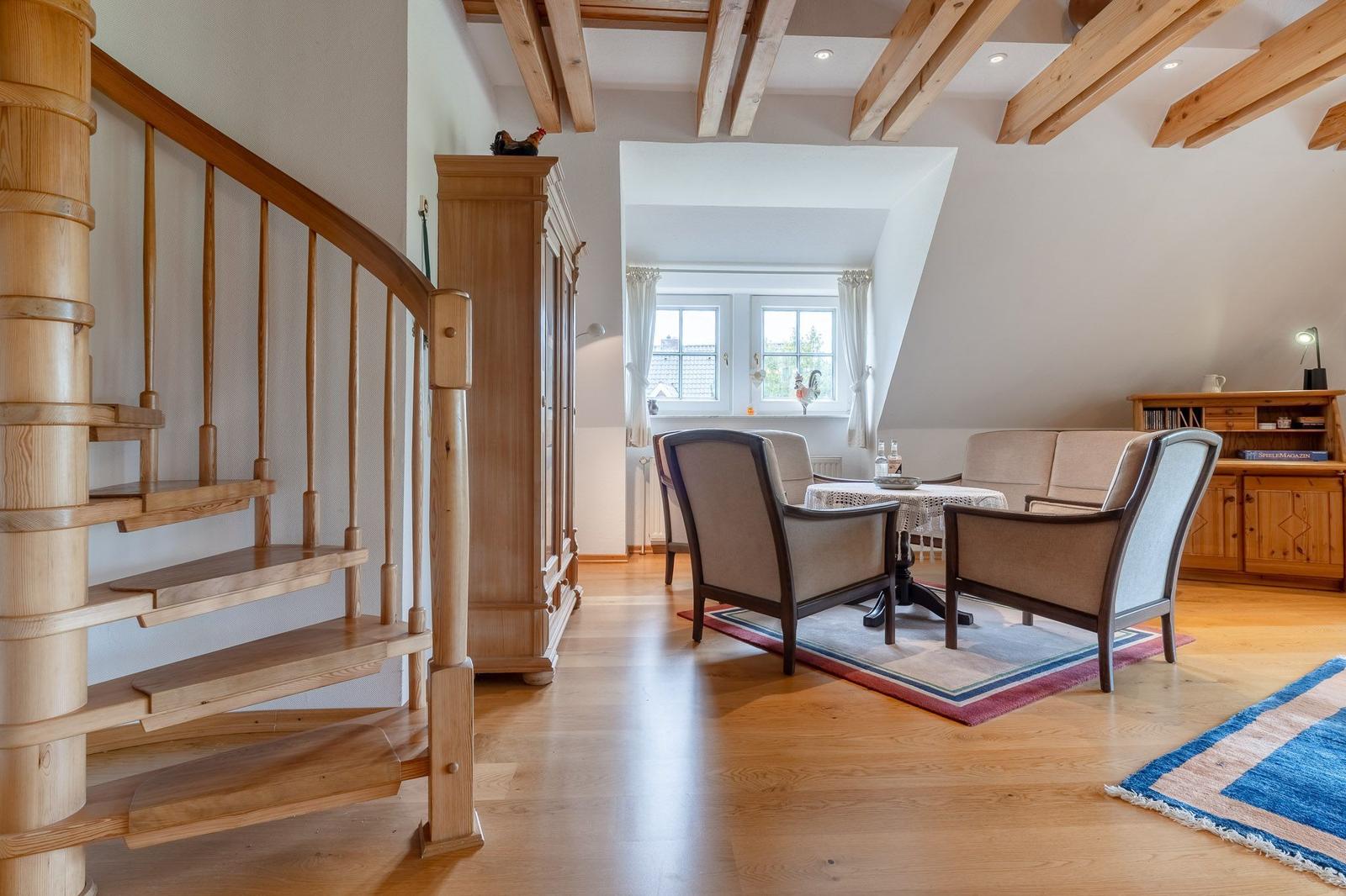 Wohnbereich mit Holztreppe, Sitzgelegenheiten und Fenster. Holzdeckenbalken und Parkettboden.