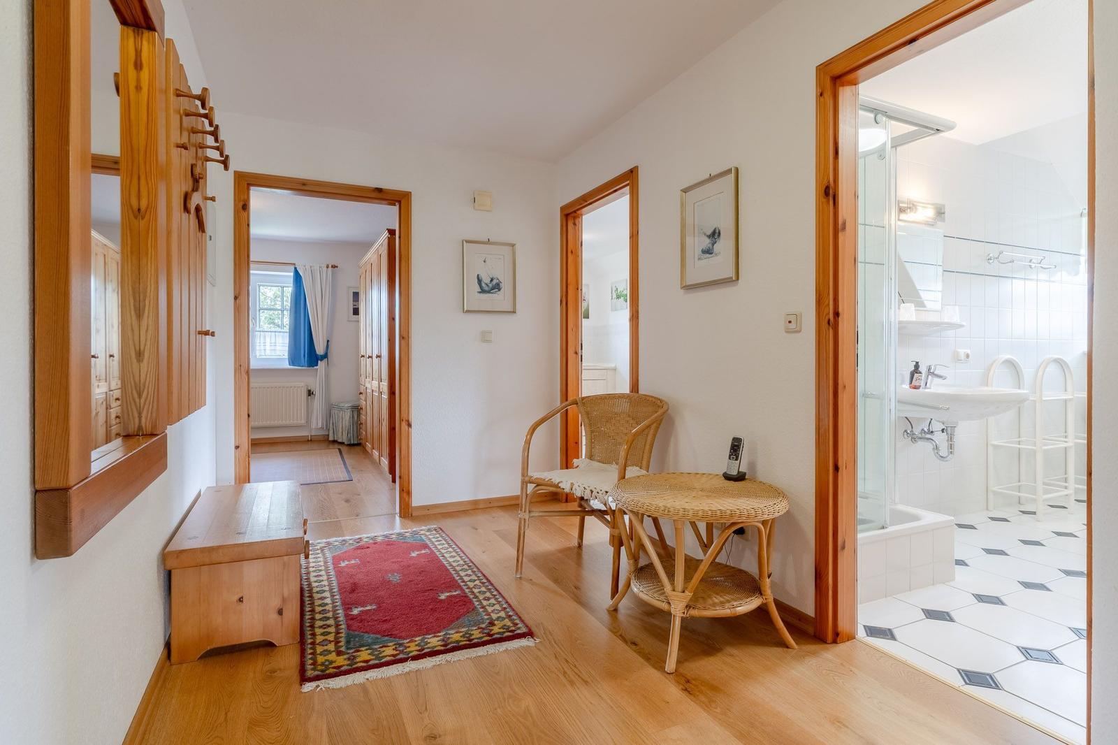 Flur mit Holzfußboden, Teppich, Stuhl und Tisch. Tür zum Bad und Schlafzimmer.