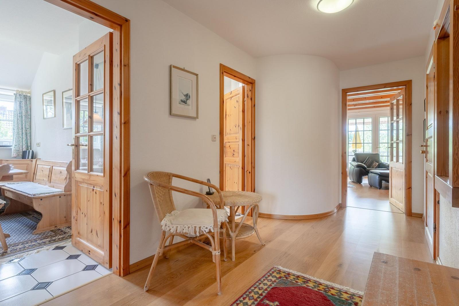 Flur mit Holztüren und Sitzgelegenheit. Blick in Küche und Wohnzimmer.