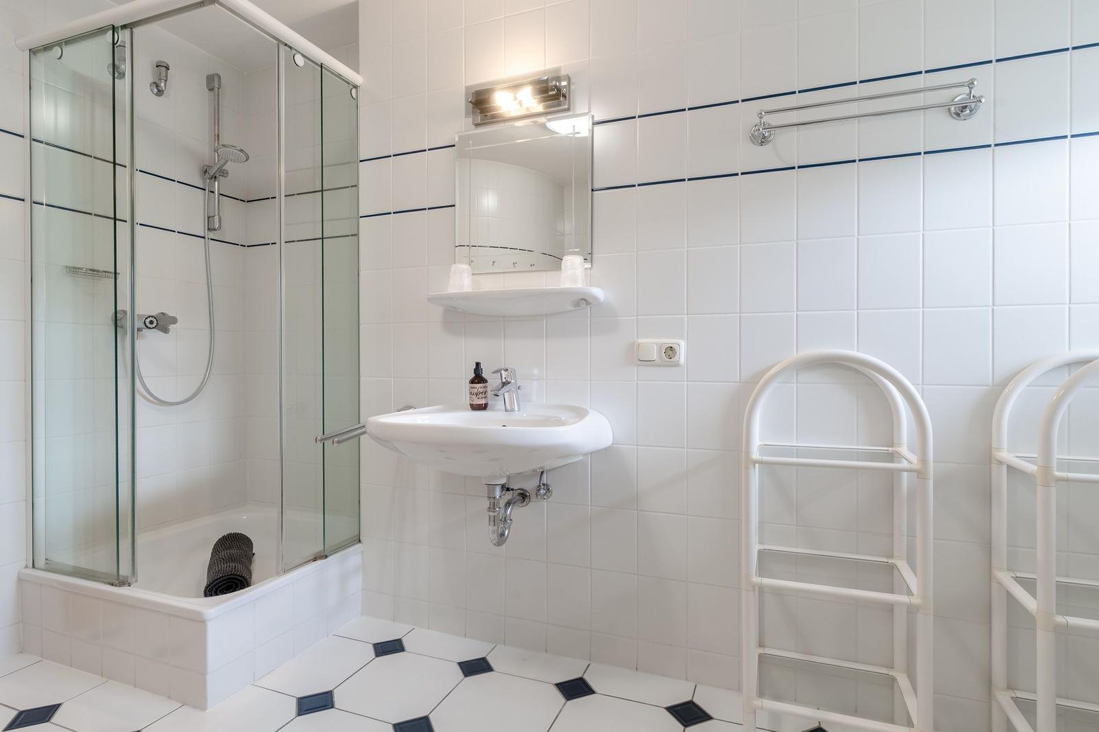 Badezimmer mit Dusche, Waschbecken und Handtuchständern.
