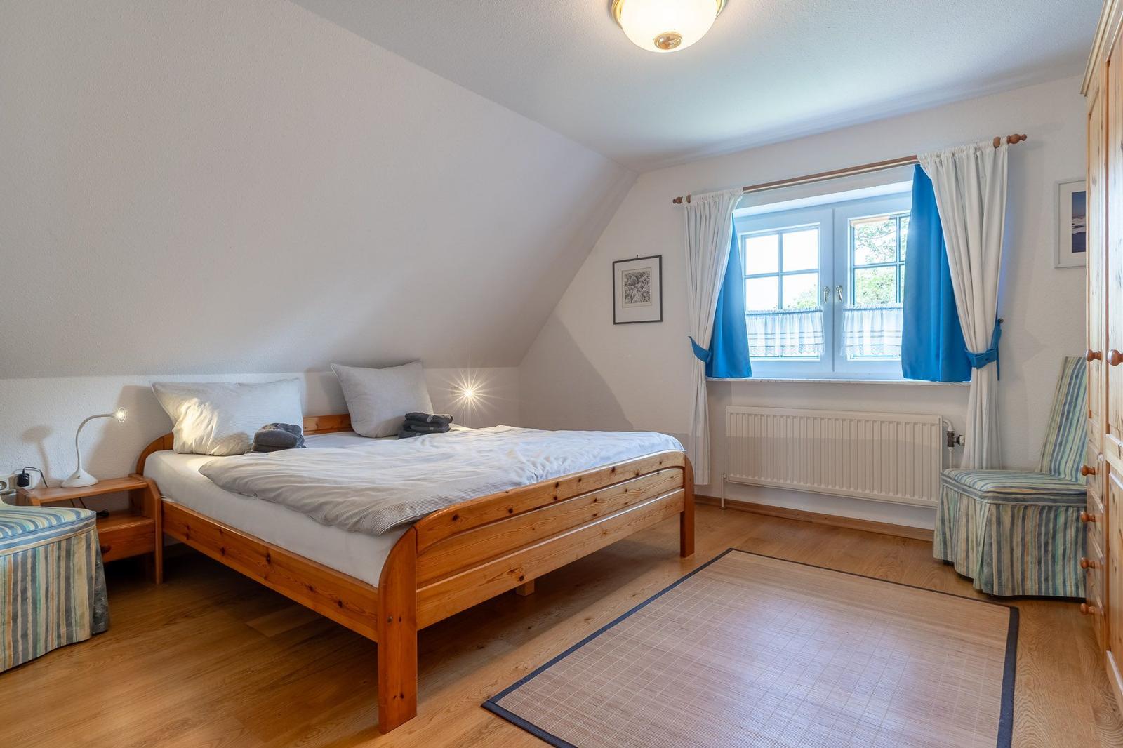 Schlafzimmer mit Holzbett, Fenster mit blauen Vorhängen und Holzboden.