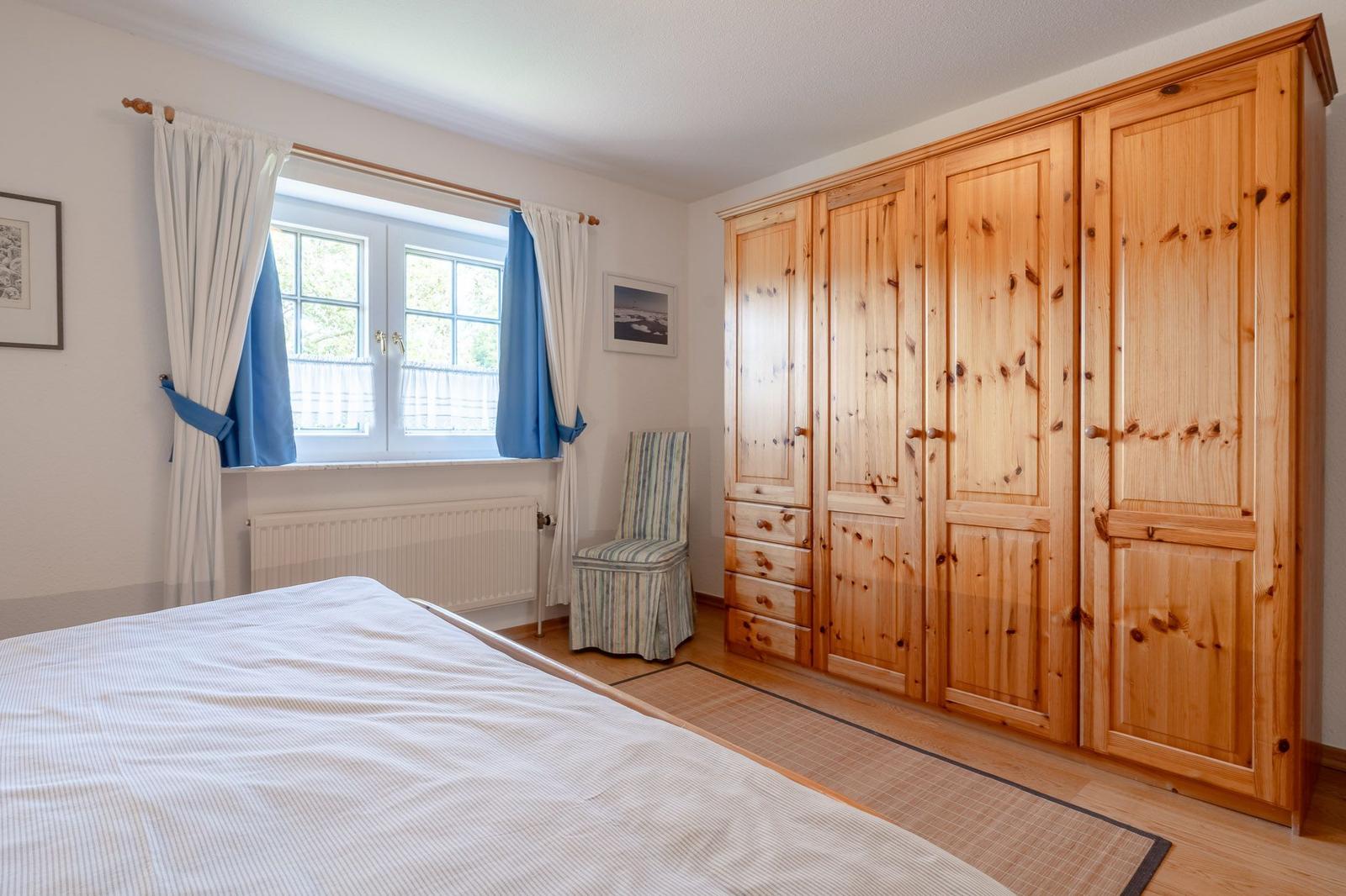 Schlafzimmer mit Holzschrank, Bett, Fenster und Stuhl.