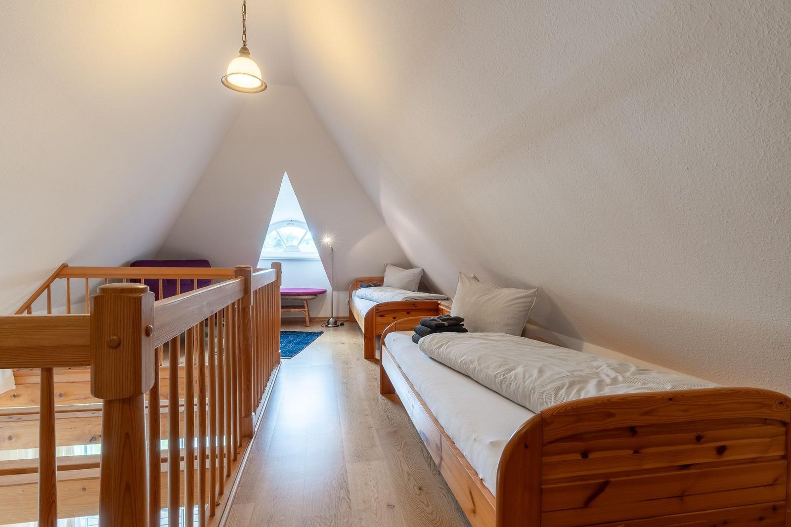 Zimmer mit zwei Betten, Holzbalken und Dachschräge. Fenster mit Sitzbank.