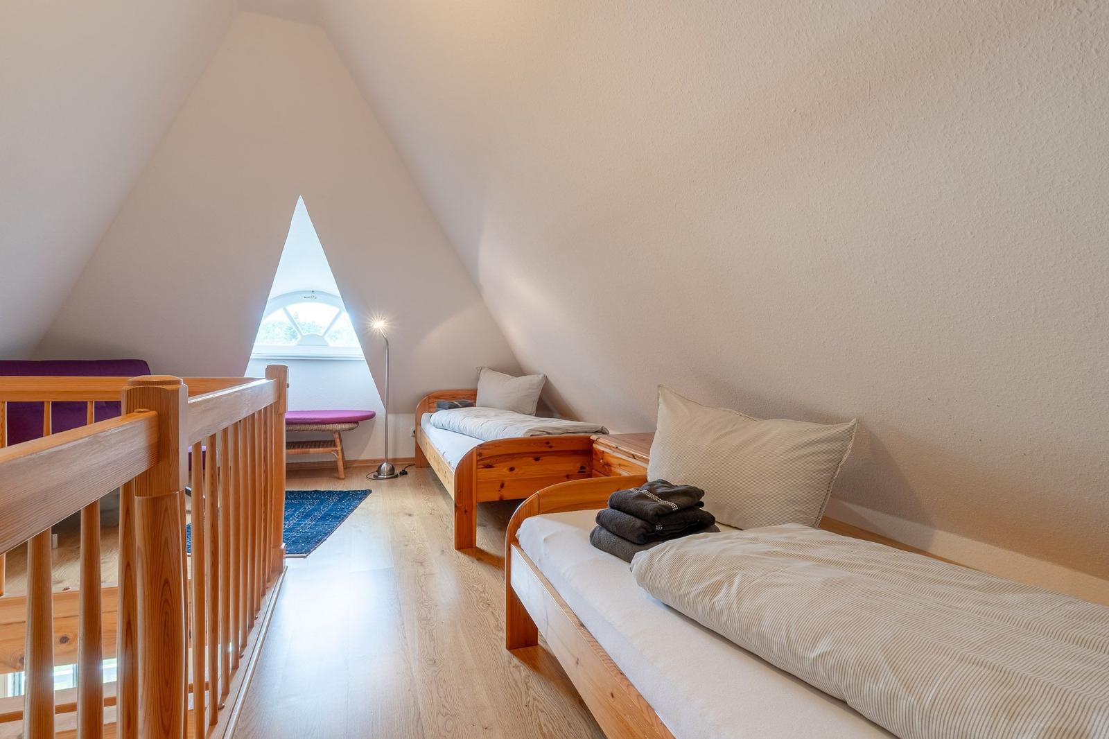 Zwei Betten unter einem Dachfenster mit Holzbalken und einem Bodenbelag.