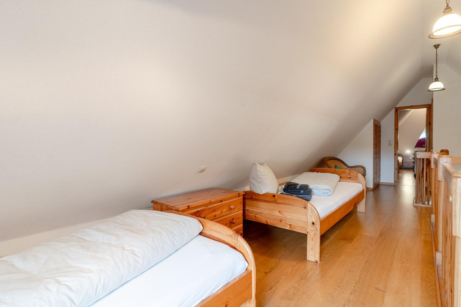 Zwei Betten mit Holzrahmen und weißer Bettwäsche in einem Dachzimmer mit Holzboden und Schiebefenster.