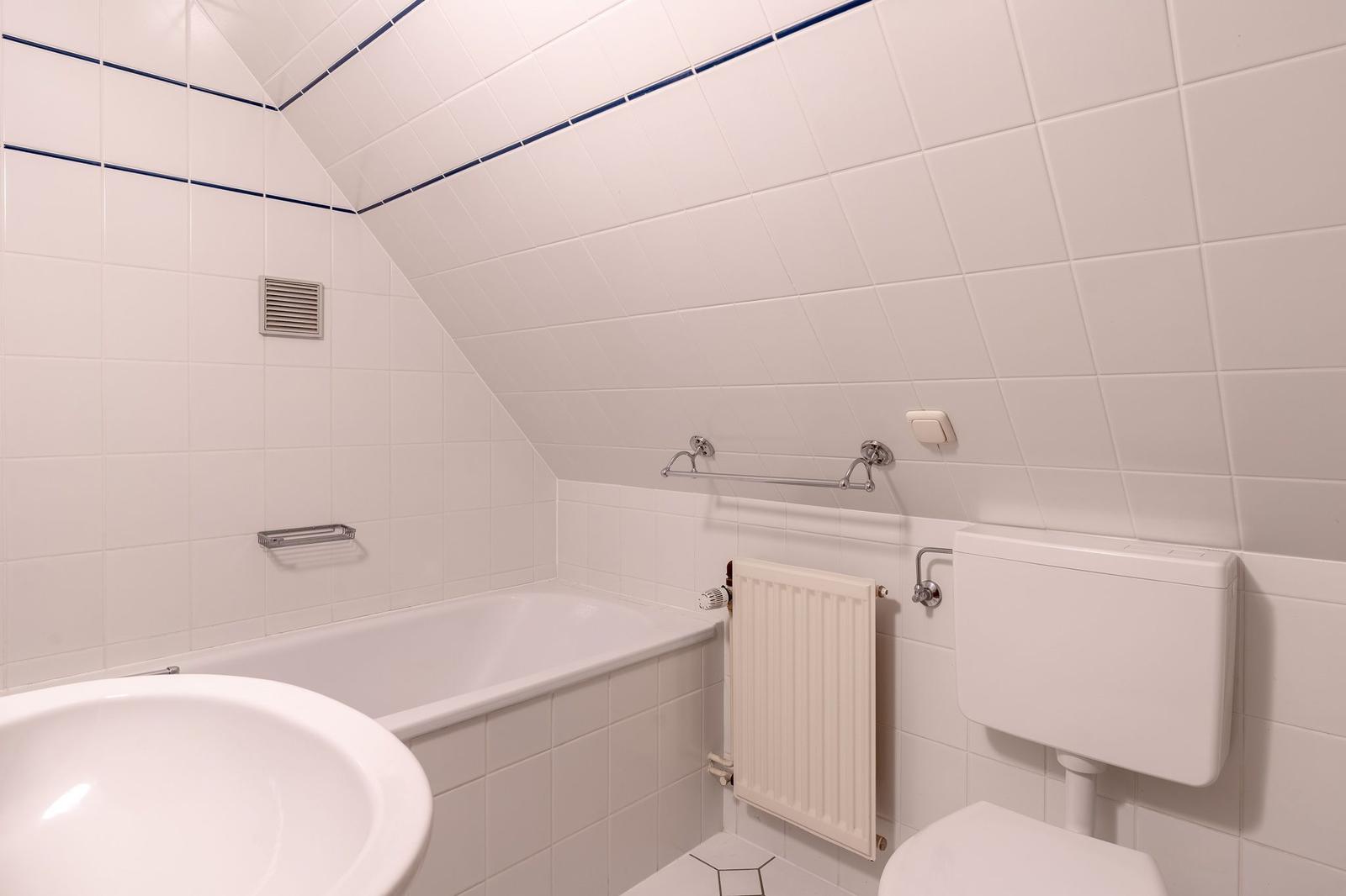 Badezimmer mit Badewanne, Waschbecken und Toilette. Weiße Fliesen mit blauer Bordüre.