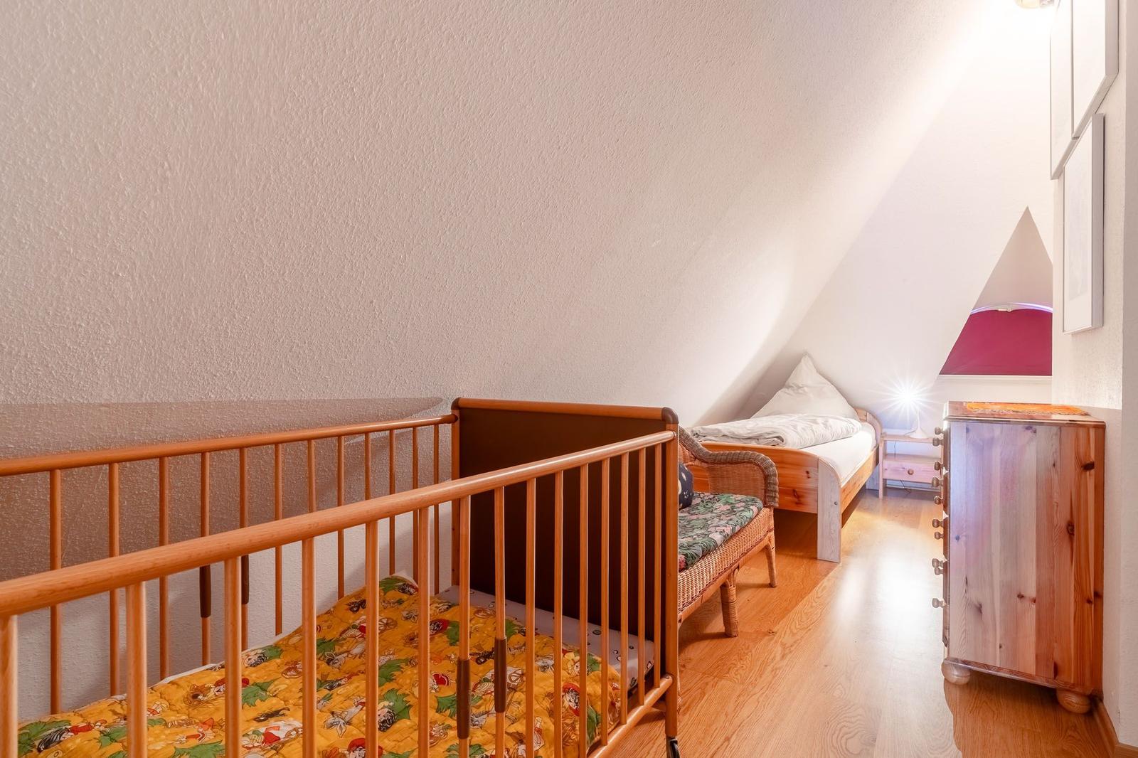Kinderzimmer mit Babybett, Bett und Schrank unter Dachschräge.