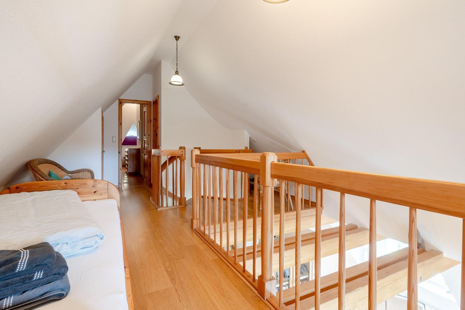 Dachgeschoss mit Holzbett, Treppenhaus und Sessel. Holzfußboden und weiße Wände.