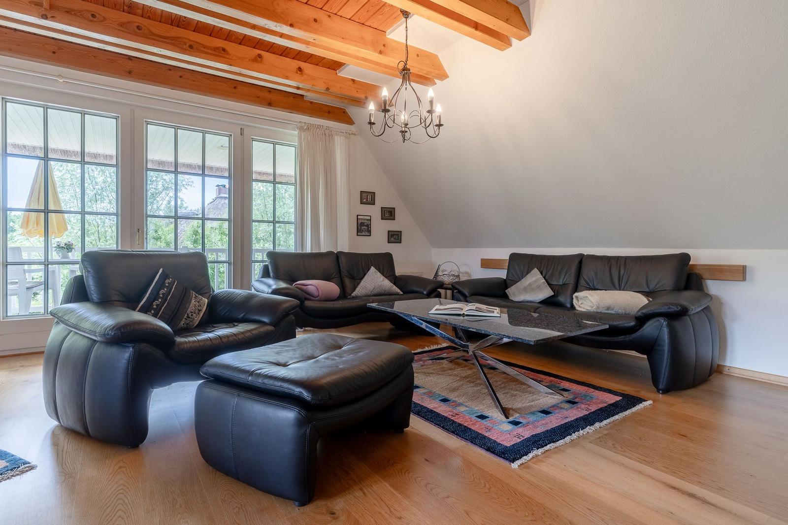 Wohnzimmer mit schwarzen Ledermöbeln, Holzboden und Holzbalken an der Decke.