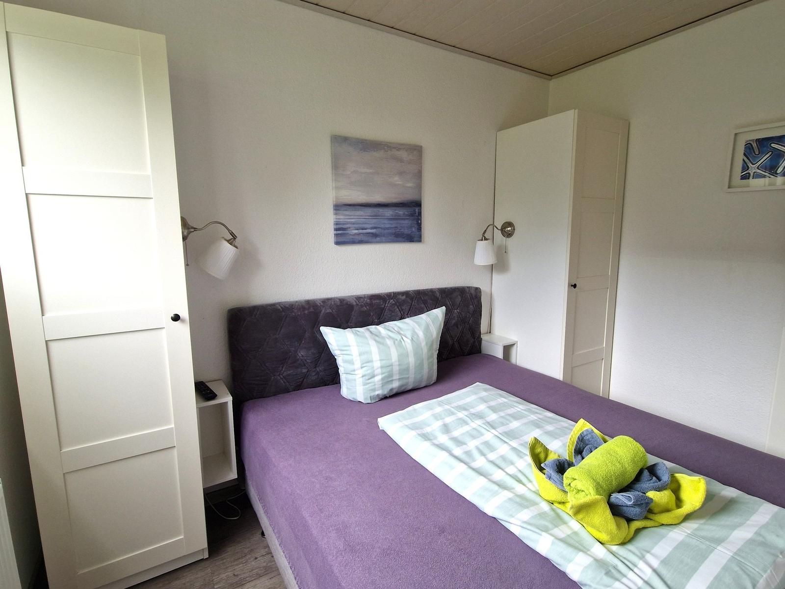 Schlafzimmer mit Bett, Nachttisch, Wandlampen und Gemälden an den Wänden.