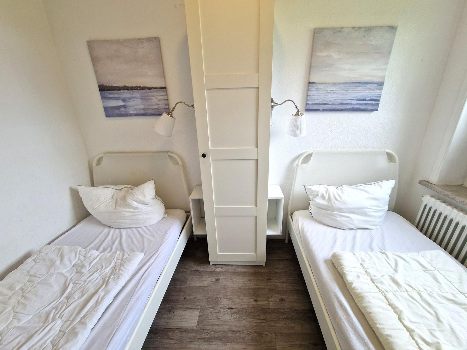 Zwei Einzelbetten mit weißen Laken und Kissen. Zwischen ihnen steht ein weißer Schrank.