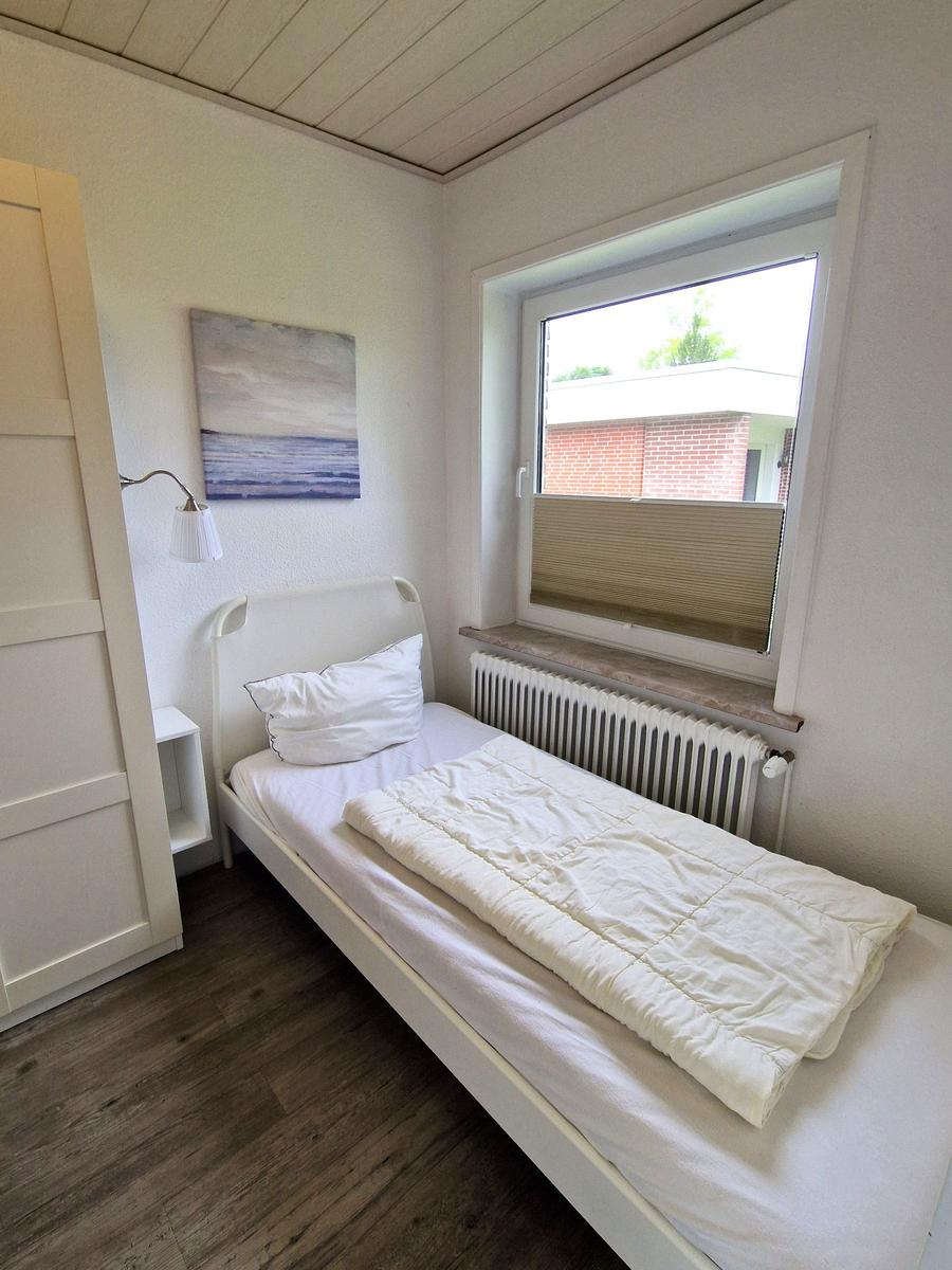 Ein Schlafzimmer mit Bett, Fenster und Wandbild. Holzfußboden und weißer Schrank.