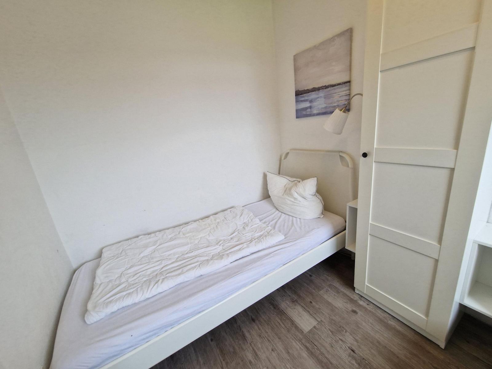 Ein Schlafzimmer mit weißem Bett, Wandbild und Schrank.