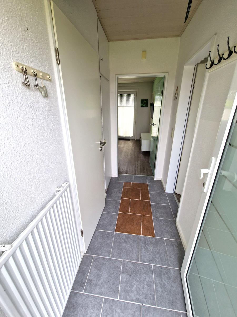 Flur mit grauen und braunen Fliesen, weißen Türen und Heizkörper an der Wand.