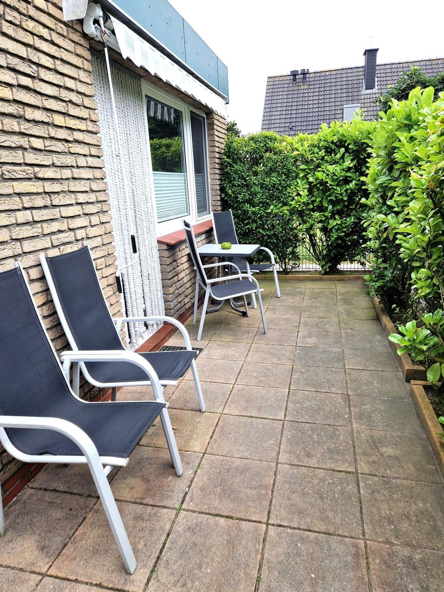 Terrasse mit zwei Liegestühlen und Tisch, umgeben von grünen Hecken.