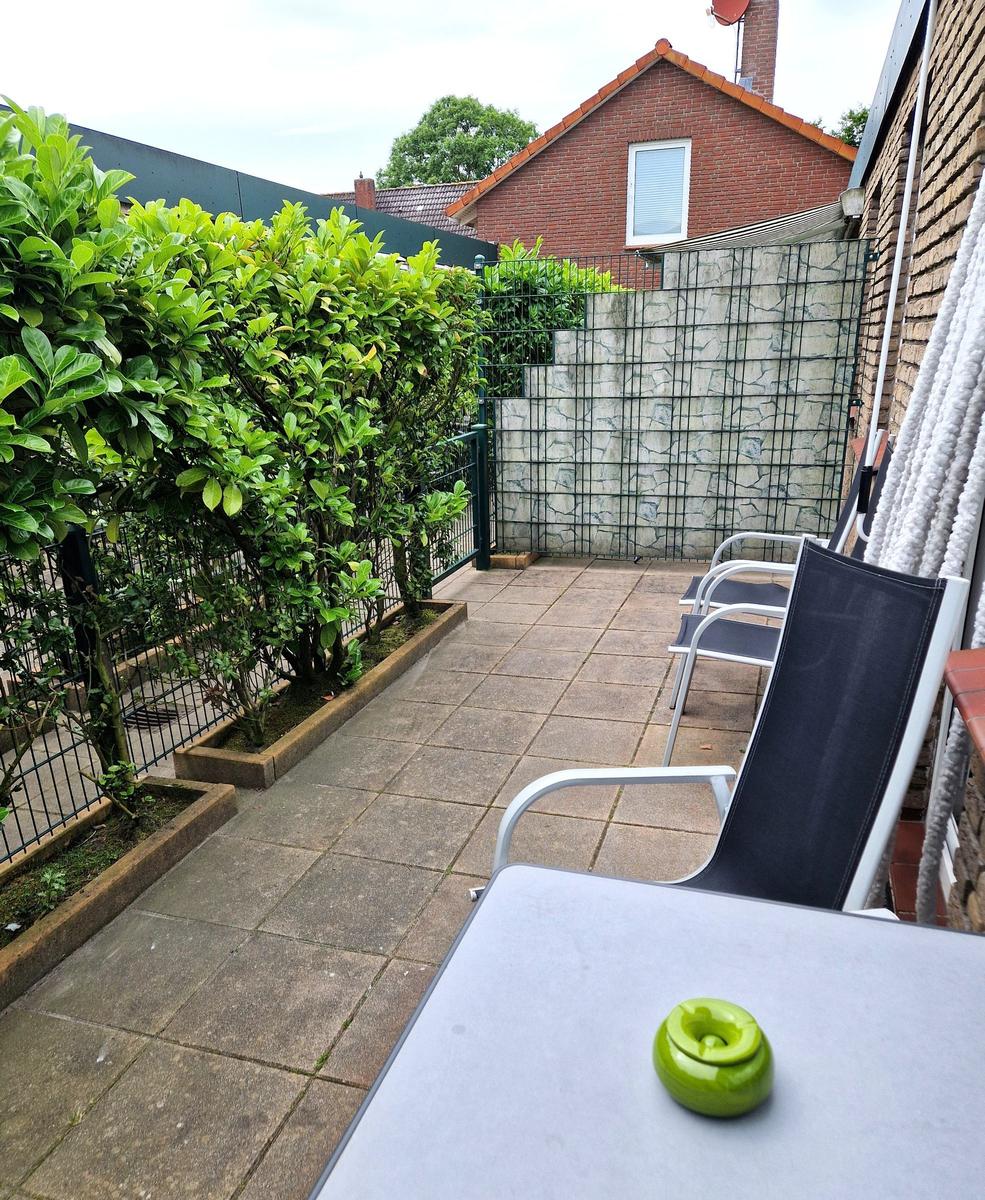 Terrasse mit Sitzgelegenheiten, Beeren und Pflanzen. Hinterhof mit Zaun und Nachbarhaus.