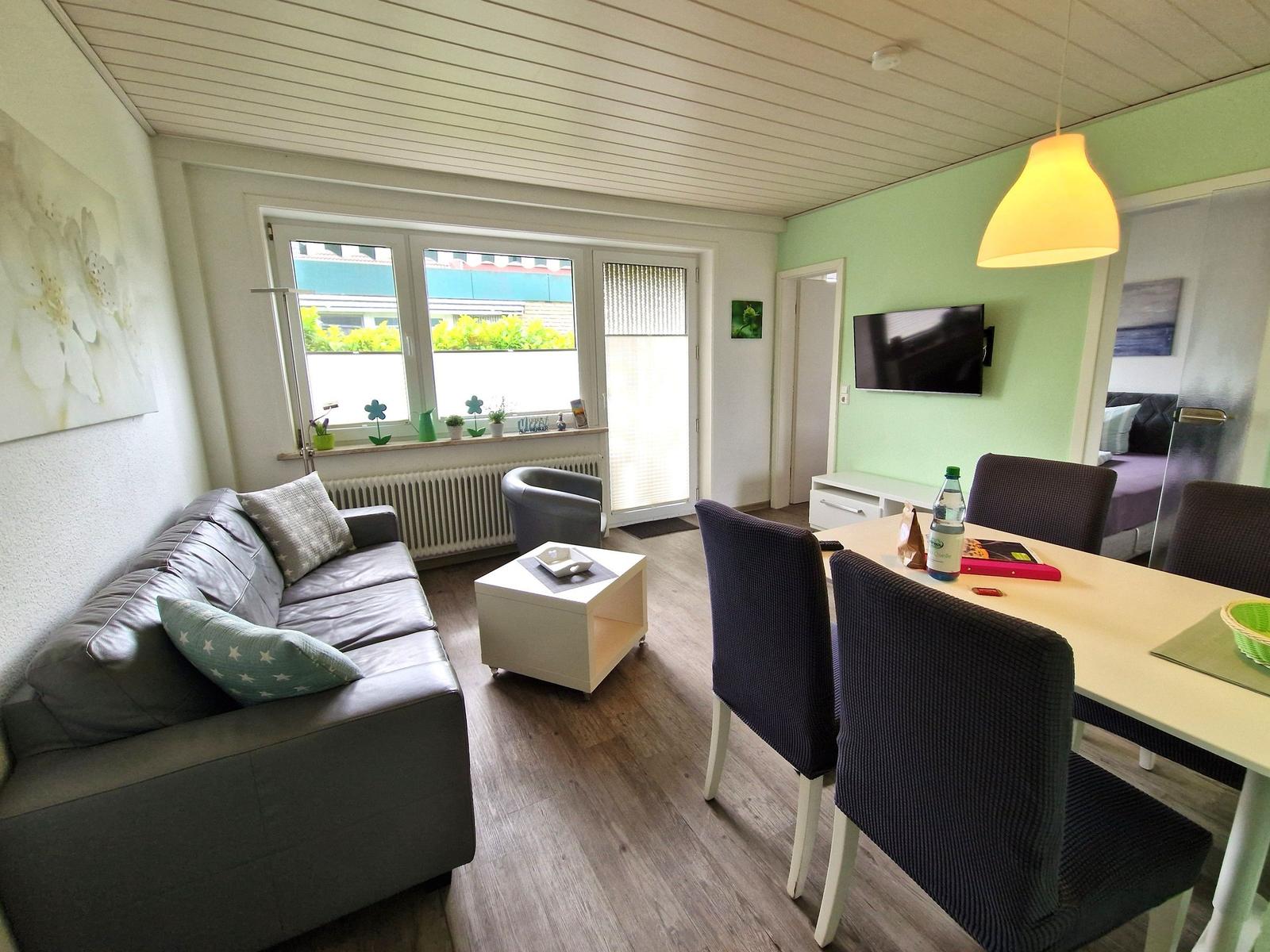 Wohn- und Essbereich mit Sofa, Esstisch und Fernseher an der Wand.