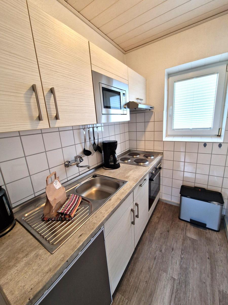 Küche mit Arbeitsplatte, Spüle, Herd, Mikrowelle und Fenster.