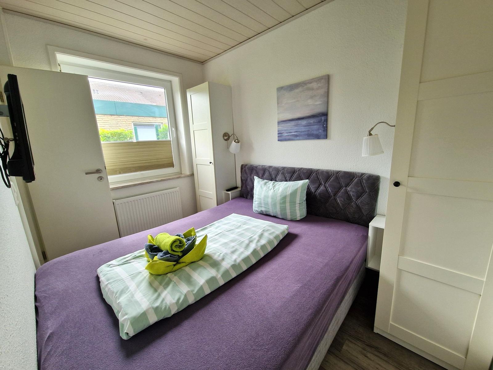 Schlafzimmer mit Bett, Fenster, Wandbild und TV.