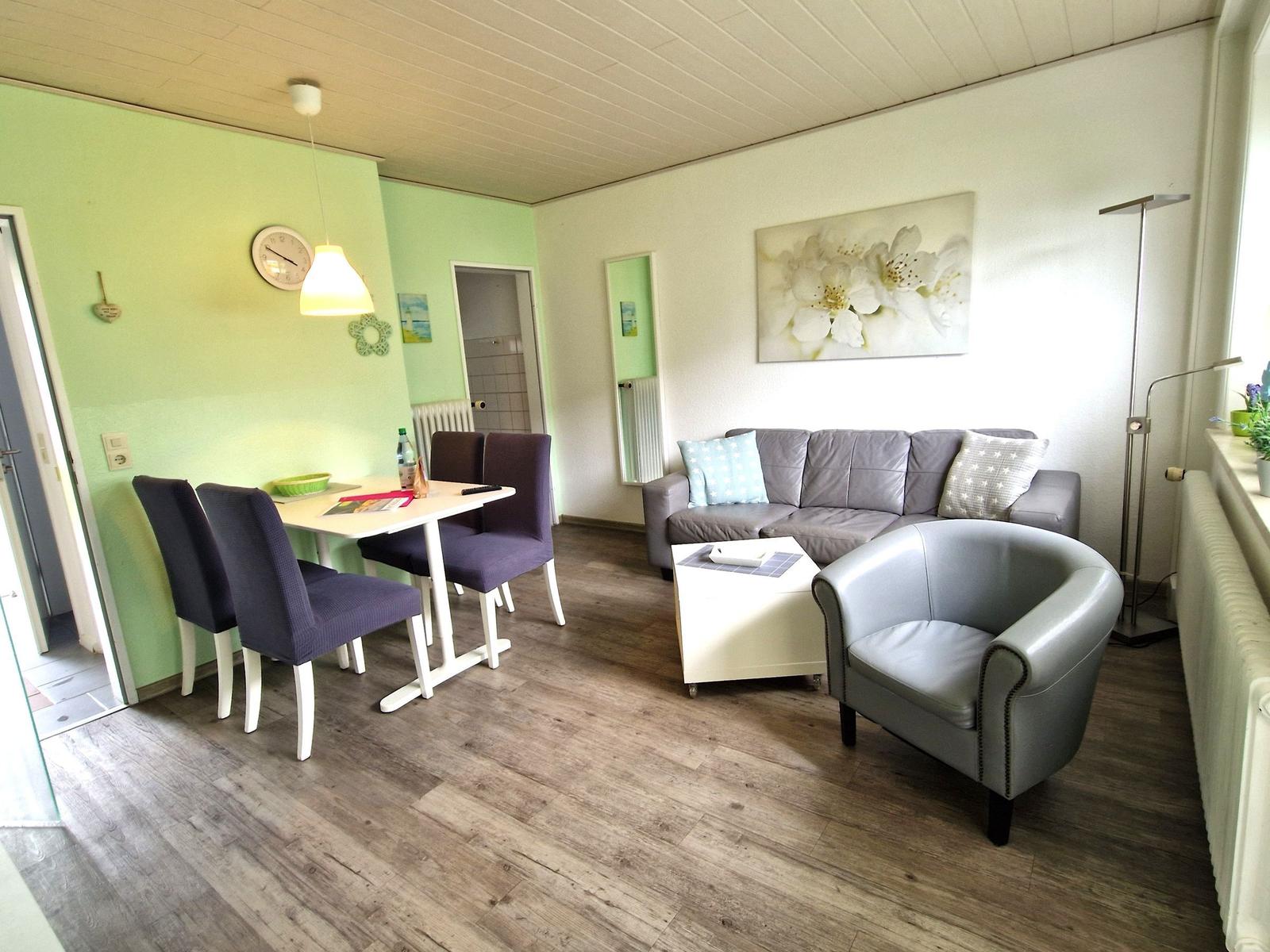 Wohn- und Essbereich mit Sofa, Sessel, Tisch und Stühlen. Wandbild und Holzboden.
