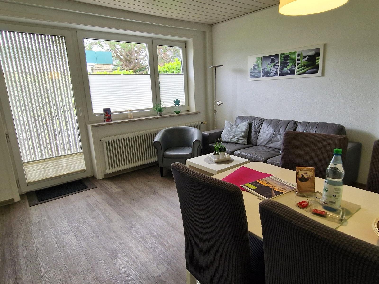Wohnzimmer mit Sofa, Sessel, Esstisch und Fenster zur Außenseite.