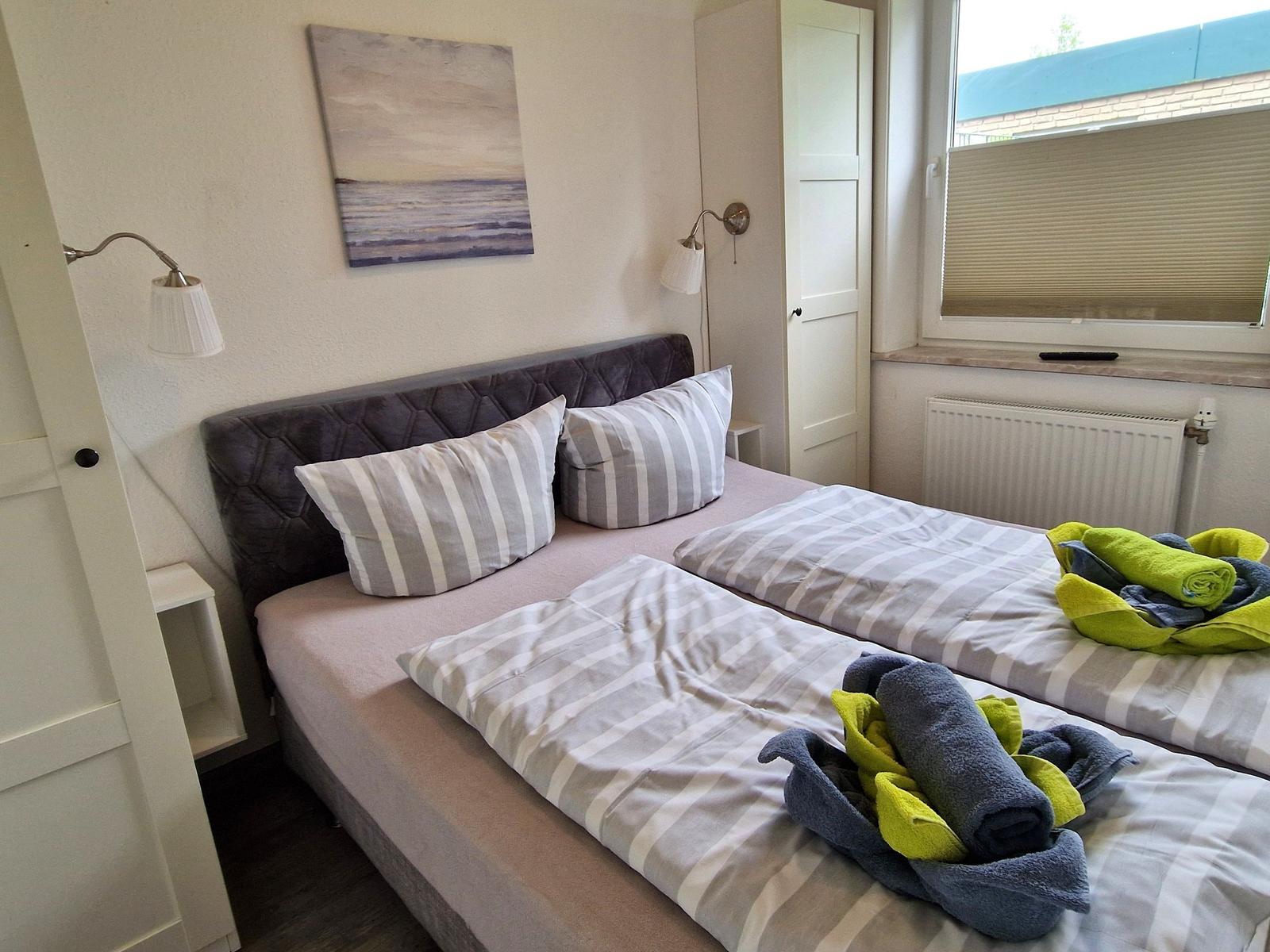 Zimmer mit Doppelbett, Wandbild und Fenster mit Rollos.