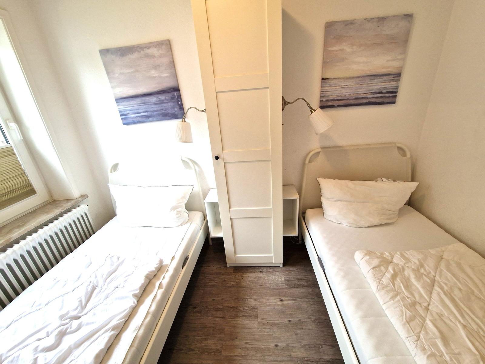 Zwei Einzelbetten mit weißen Bettwäsche, Wandbild und Schrank im Schlafzimmer.