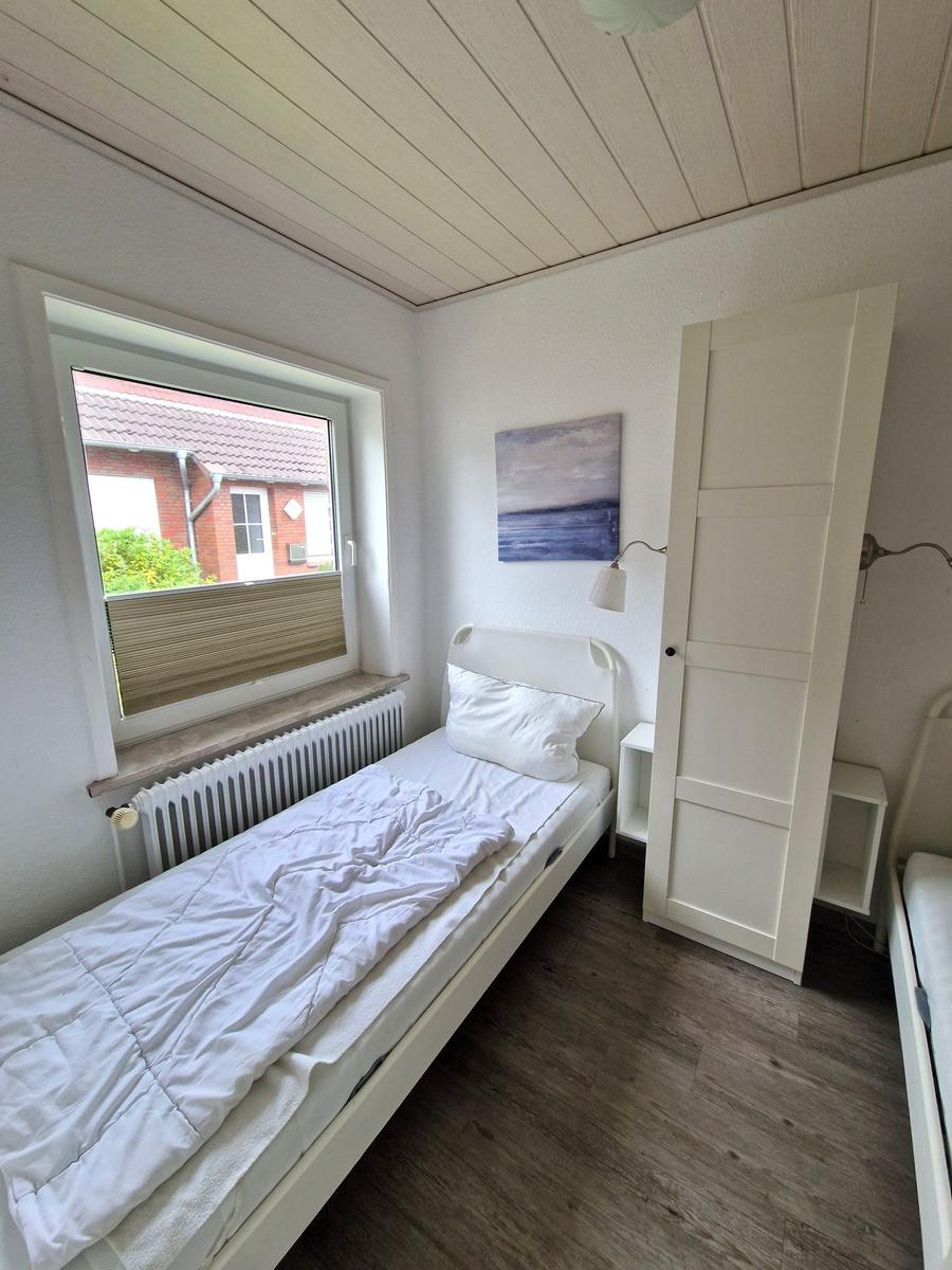 Ein Schlafzimmer mit weißem Bett, Fenster und Kleiderschrank.