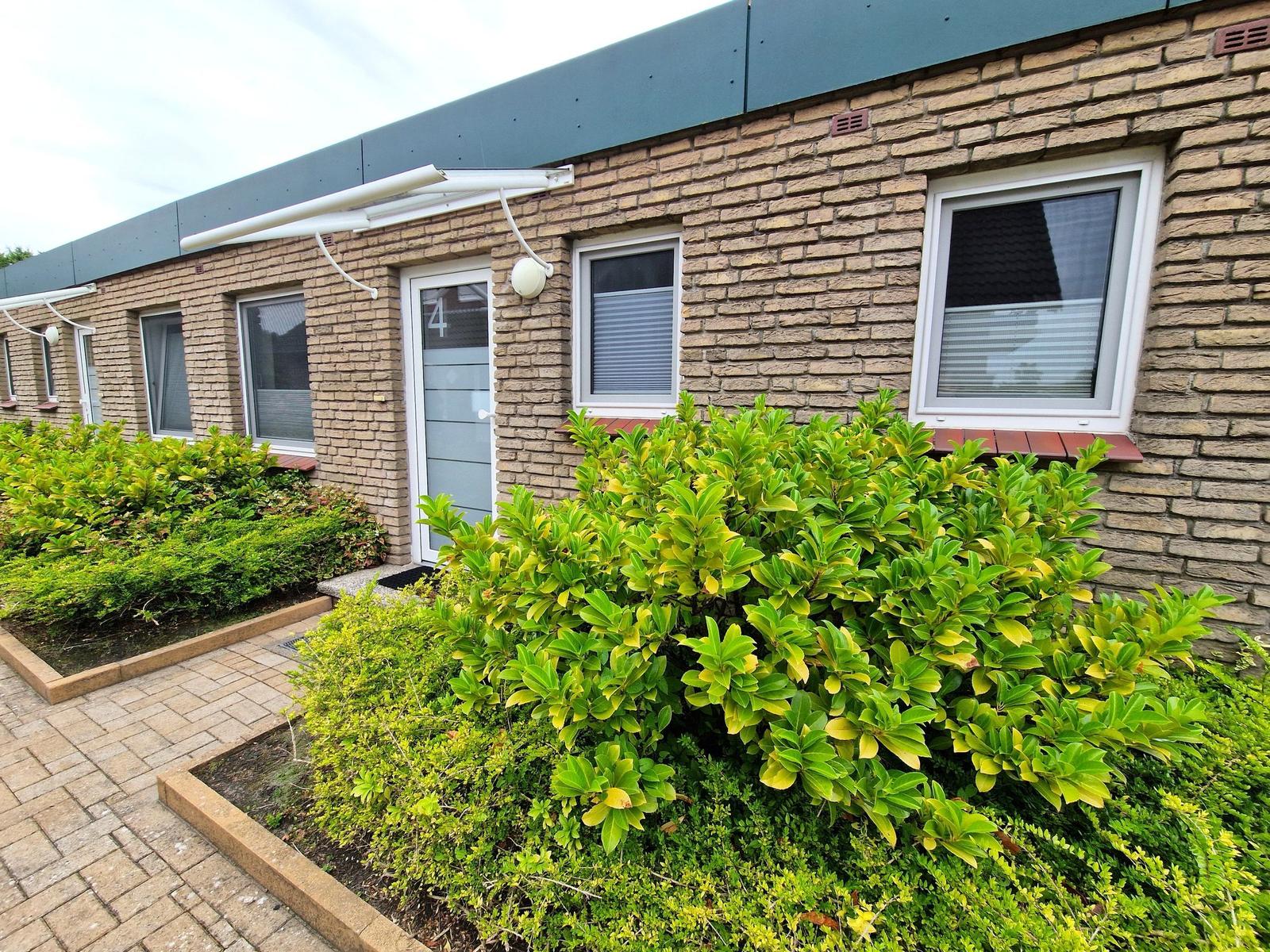 Ferienwohnung mit Steinmauer, Fenstern und grüner Vegetation vor der Tür.