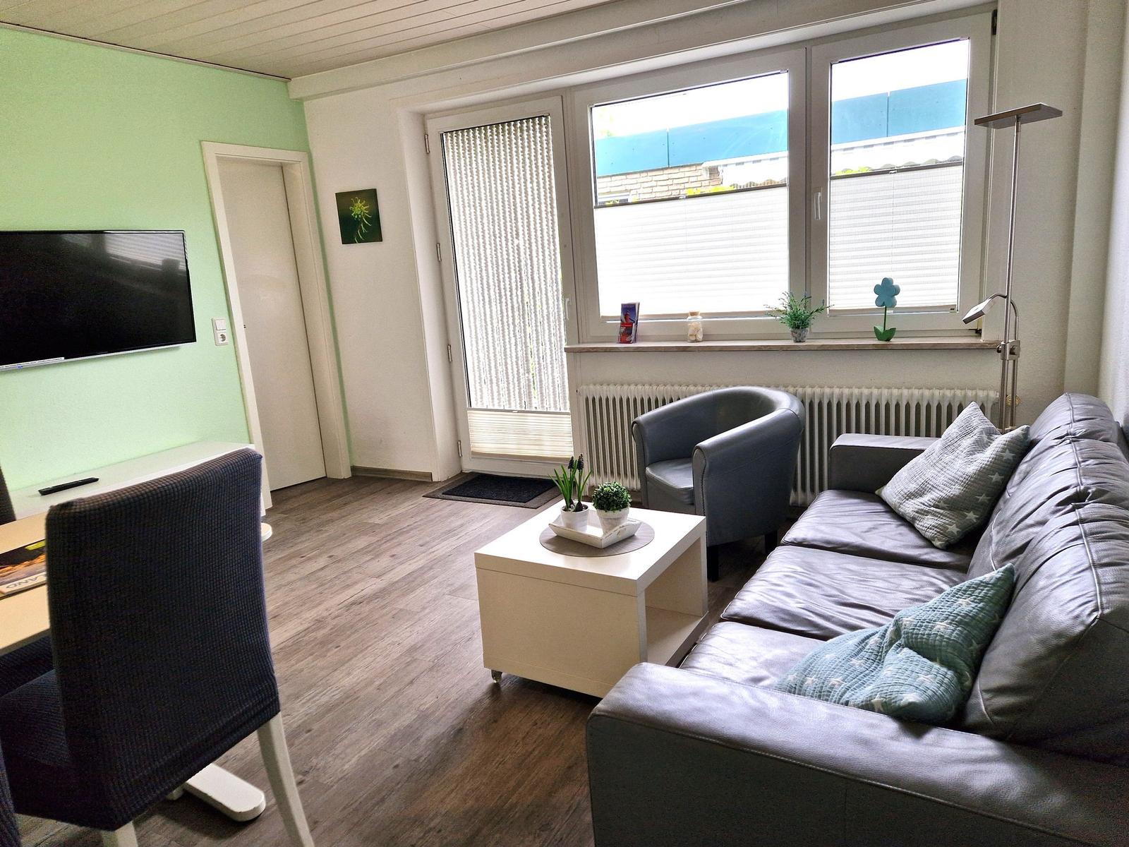 Wohnzimmer mit Sofa, Sessel, Couchtisch und Fernseher an der Wand.