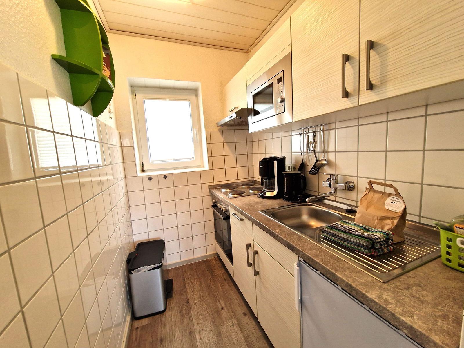 Küche mit Spüle, Herd, Kühlschrank und Mikrowelle. Wandfliesen und Holzboden.