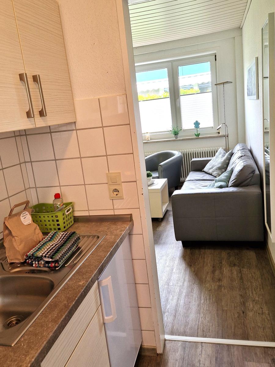 Küche mit Spüle und Arbeitsfläche. Wohnzimmer mit Sofa und Fenster.