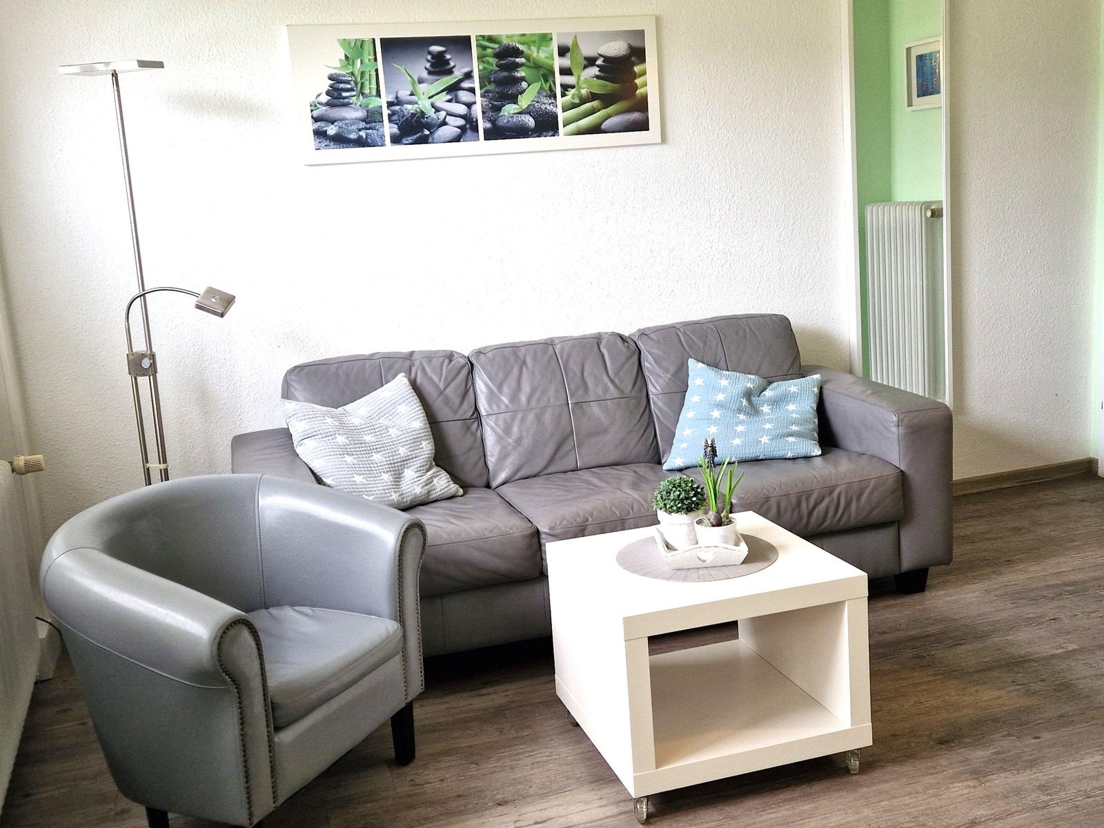 Ein Wohnzimmer mit grauem Sofa, kleinem Sessel und weißem Couchtisch.