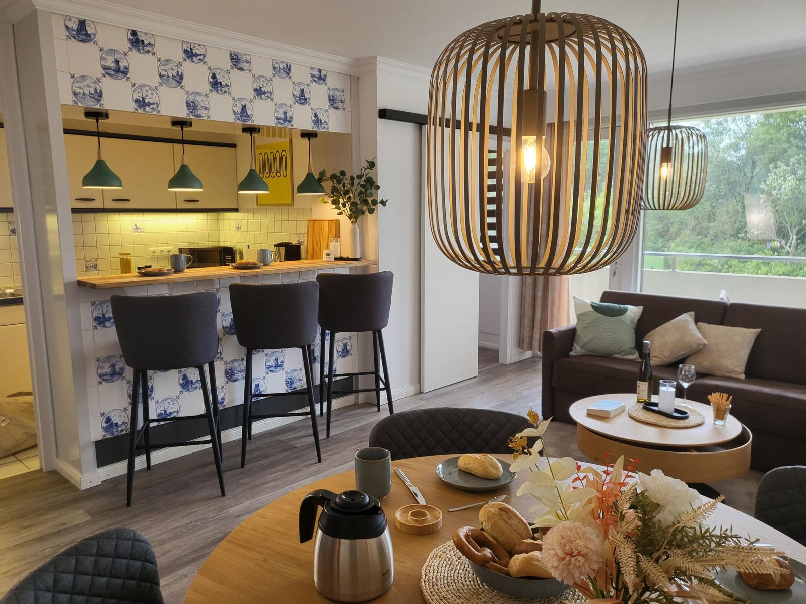 Küche mit Barhocker, Wohnbereich mit Sofa und Esstisch mit Brot.