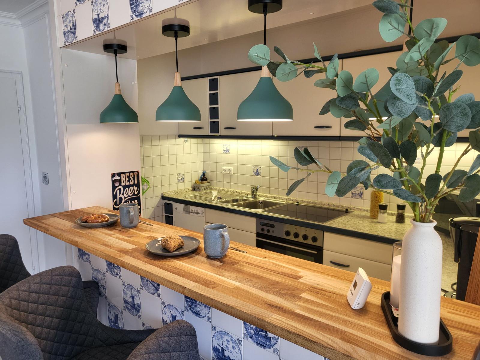 Küche mit Holzbar, grünen Hängelampen und blau-weißen Fliesen an der Wand.